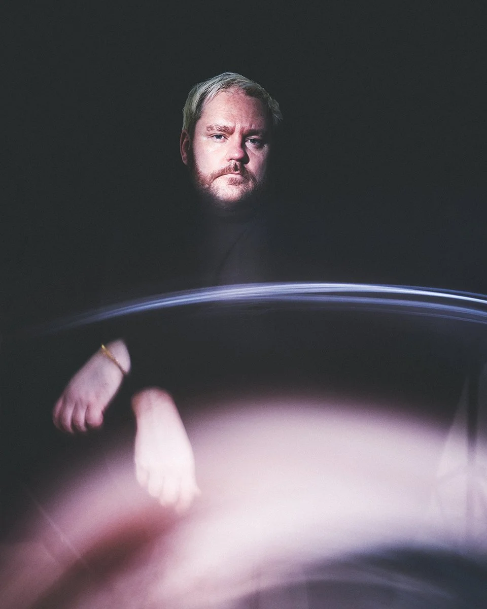 Portrait of a man with a beard and blond hair against a dark background, with motion blur and light streaks in the foreground.