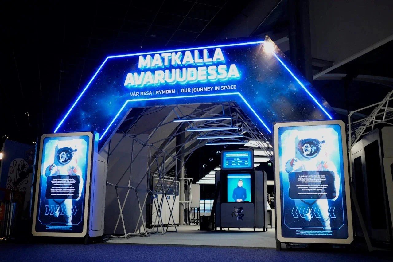 Entrance to an exhibit titled 'Matkalla Avaruudessa,' with neon blue lights, digital screens, and space-themed visuals.
