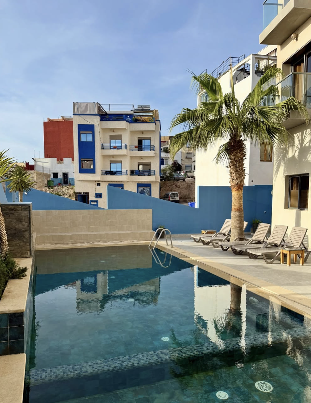 En swimmingpool i Tamraght med liggestole placeret ved siden af, hvor der kastes en skygge fra en palme