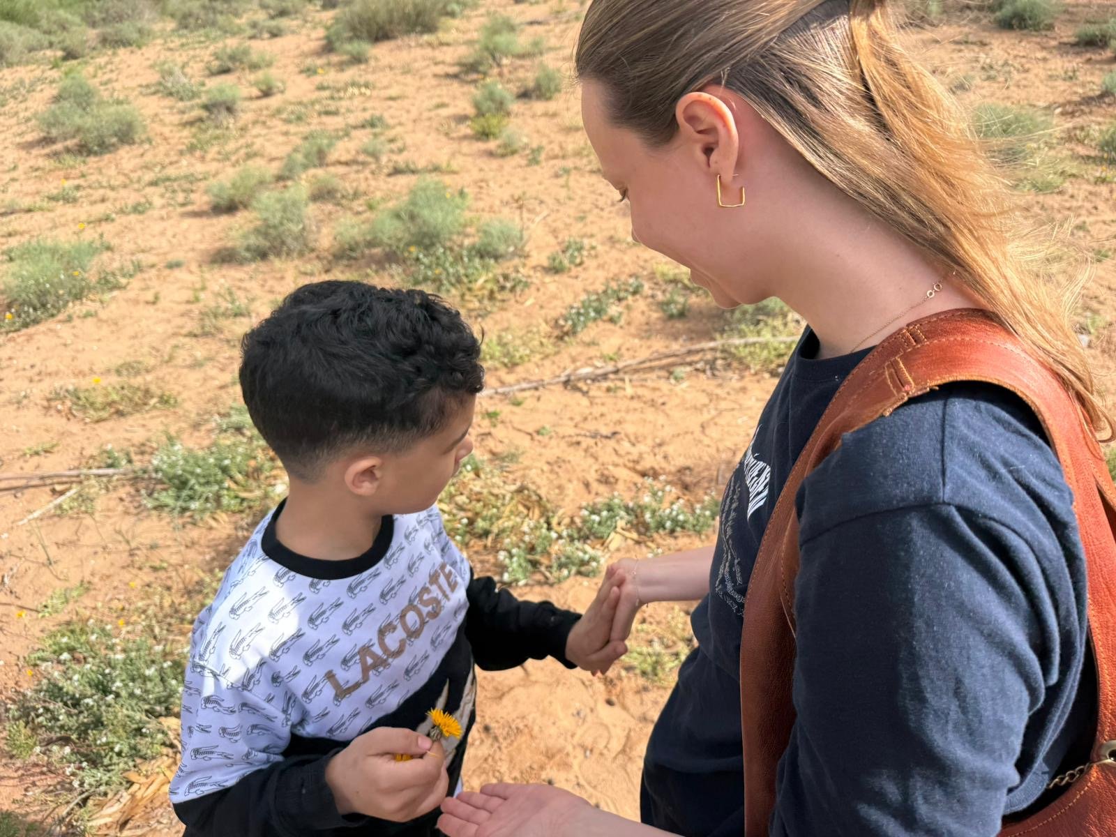 Ung pige står med lille dreng og holder i hånden udenfor i solen i Marokko.