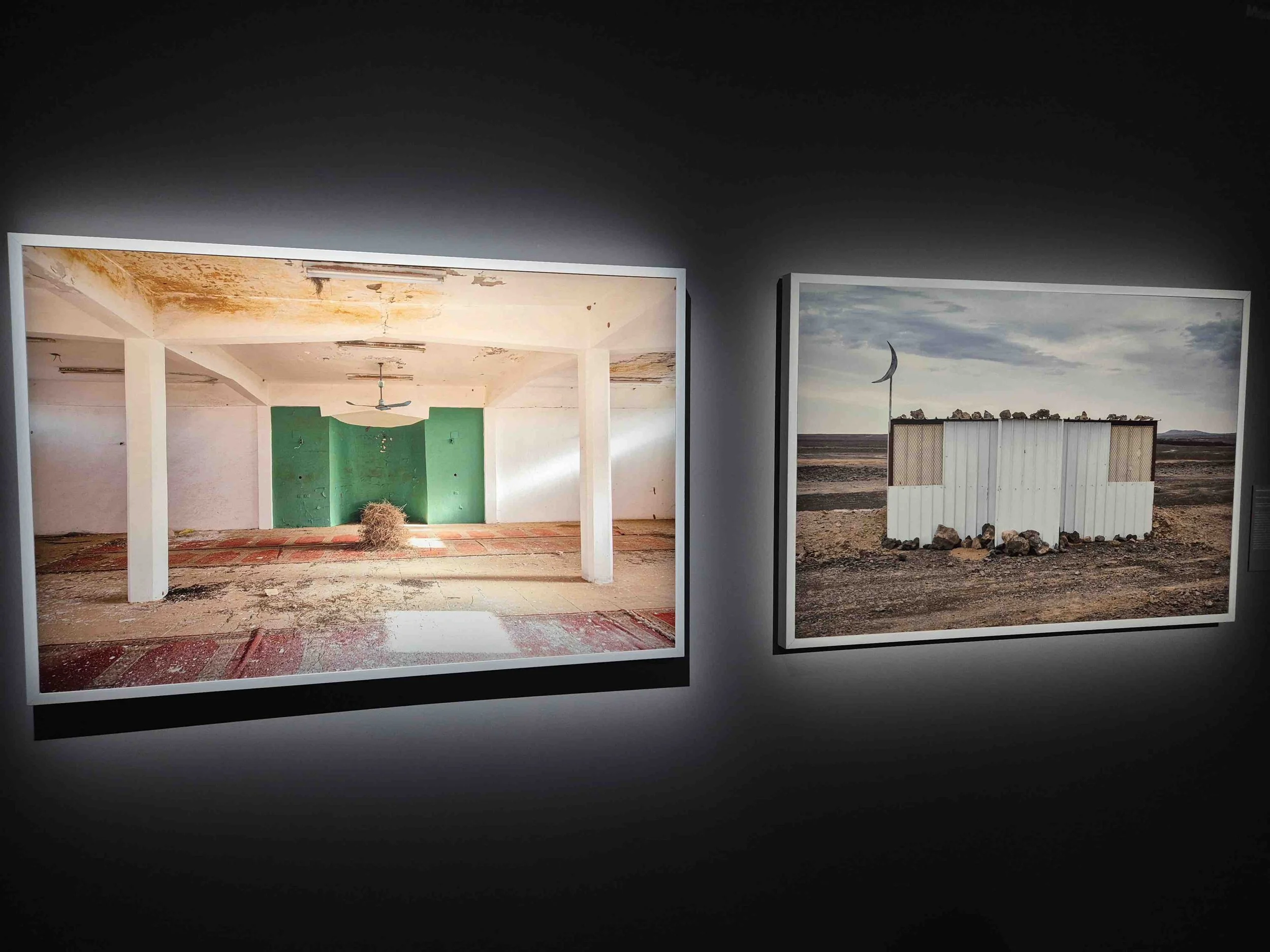 Two artworks by Saudi artist Moath Alofi showing a temporary mosque in the desert with peeling paint, a green accent wall, and a ceiling fan. The right photo depicts a a structure made of white panels, a flagpole with a crescent-shaped flag,.