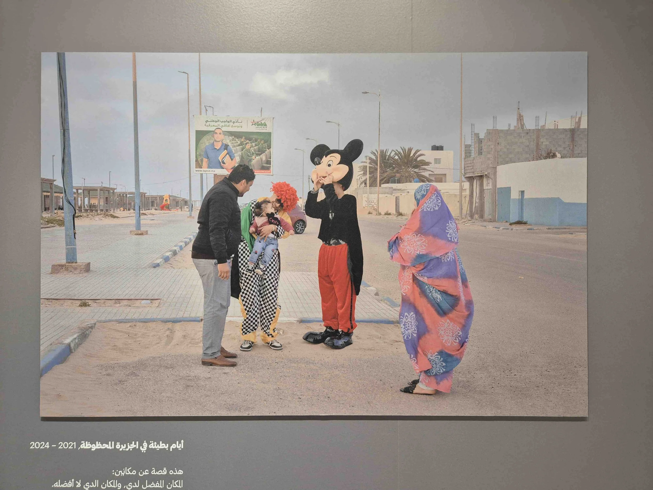 People in costumes in Tangier, Morroco, including a person dressed as Minnie Mouse, are standing on a street with some buildings in the background. One person is holding a child, and another woman is wearing a colorful headscarf. 