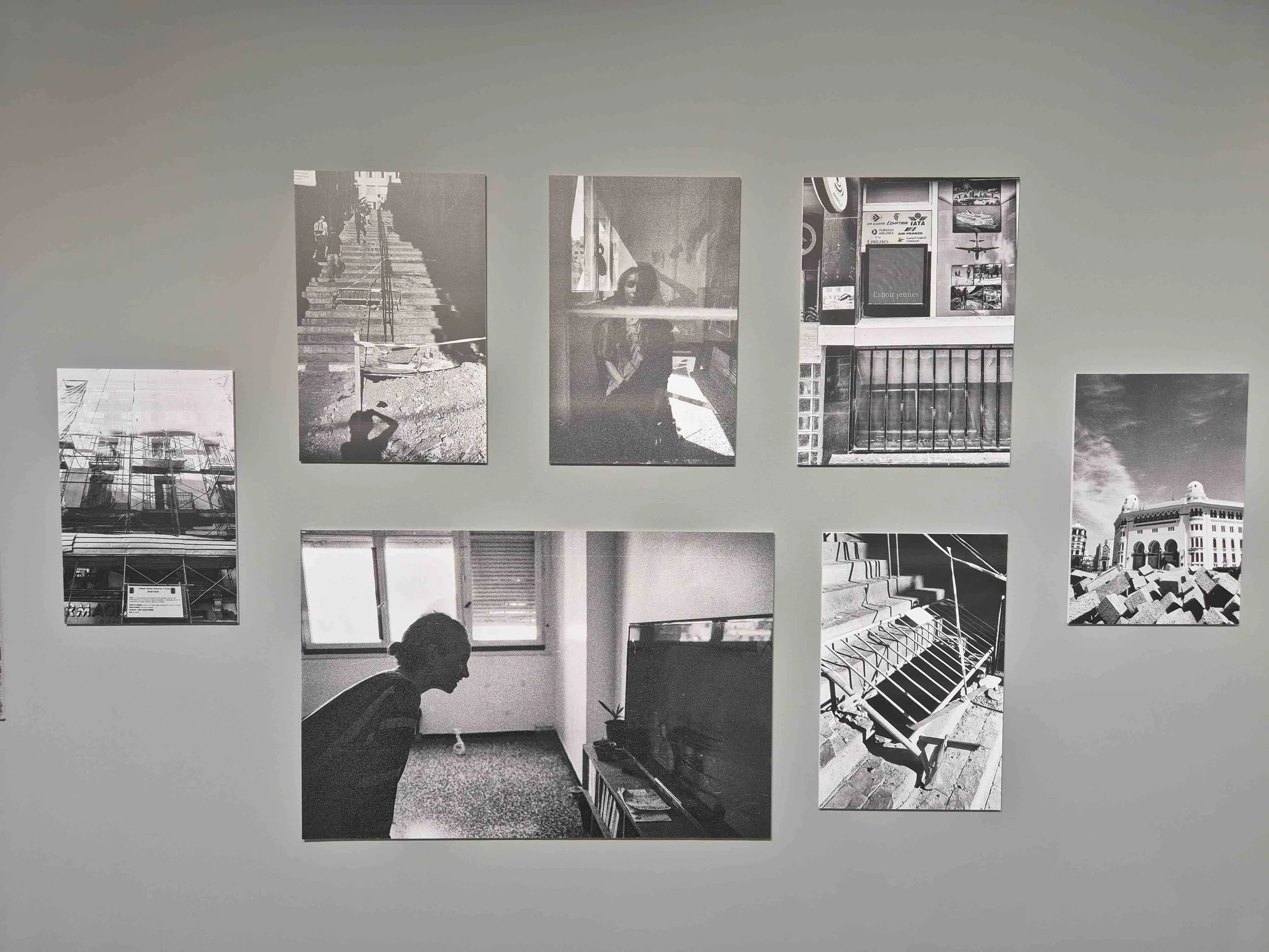 A wall display of eight black and white photographs, including images of architecture, urban scenes, and a person in a room.