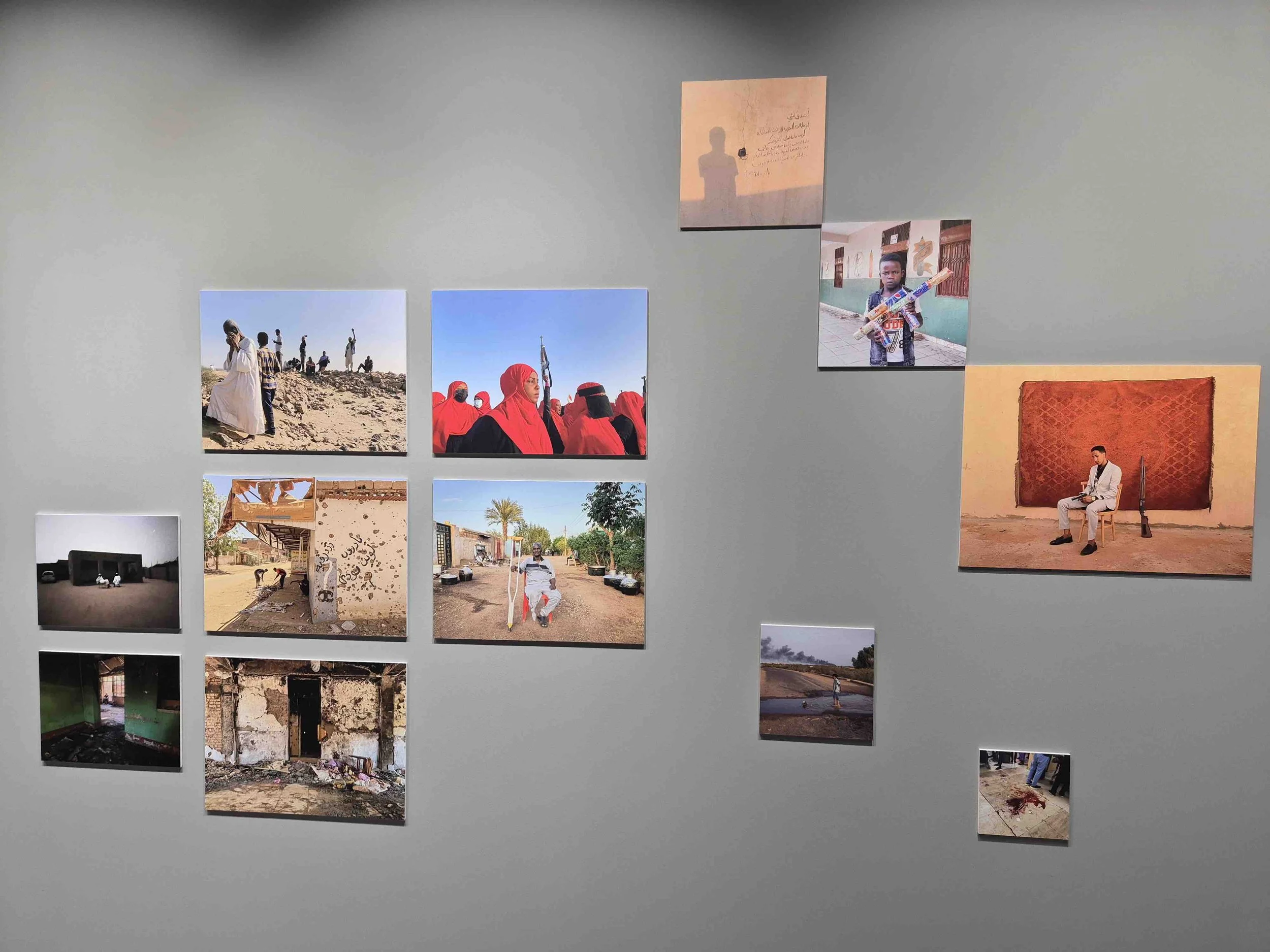 A collage of photographs displayed on a wall, showcasing scenes of people in traditional clothing, children, street scenes, and a seated man with a rifle.