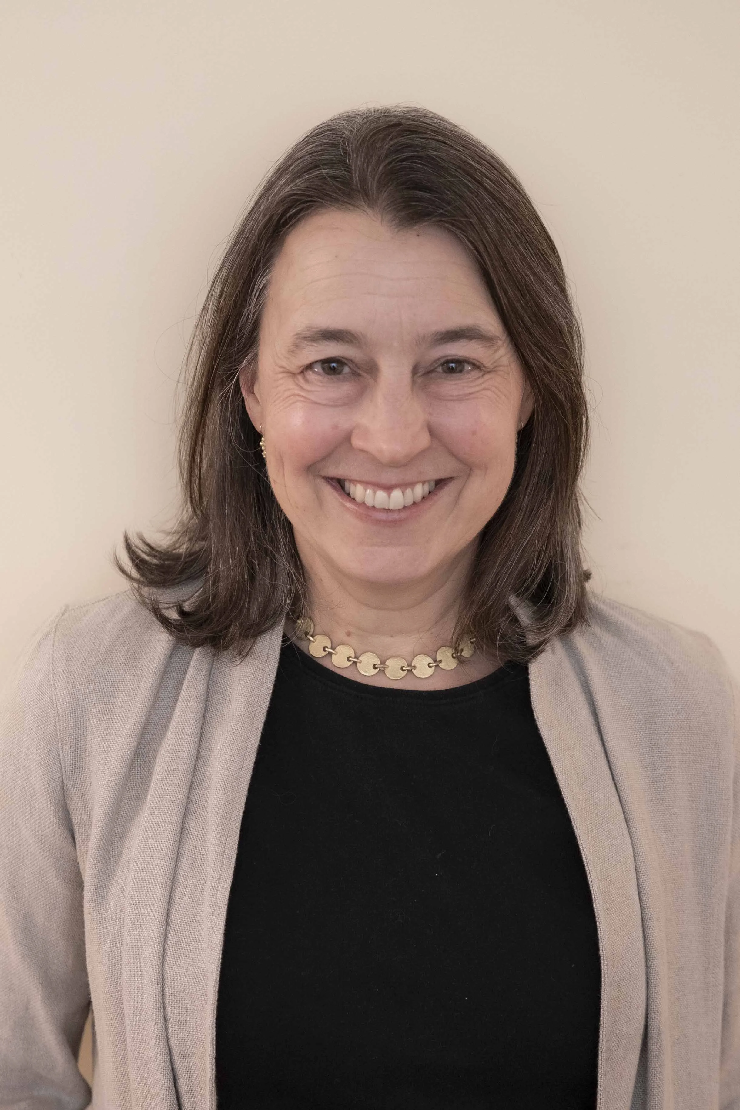 Jenny Mayher Headshot, smiling woman with shoulder length brown hair, a black shirt and oatmeal cardigan
