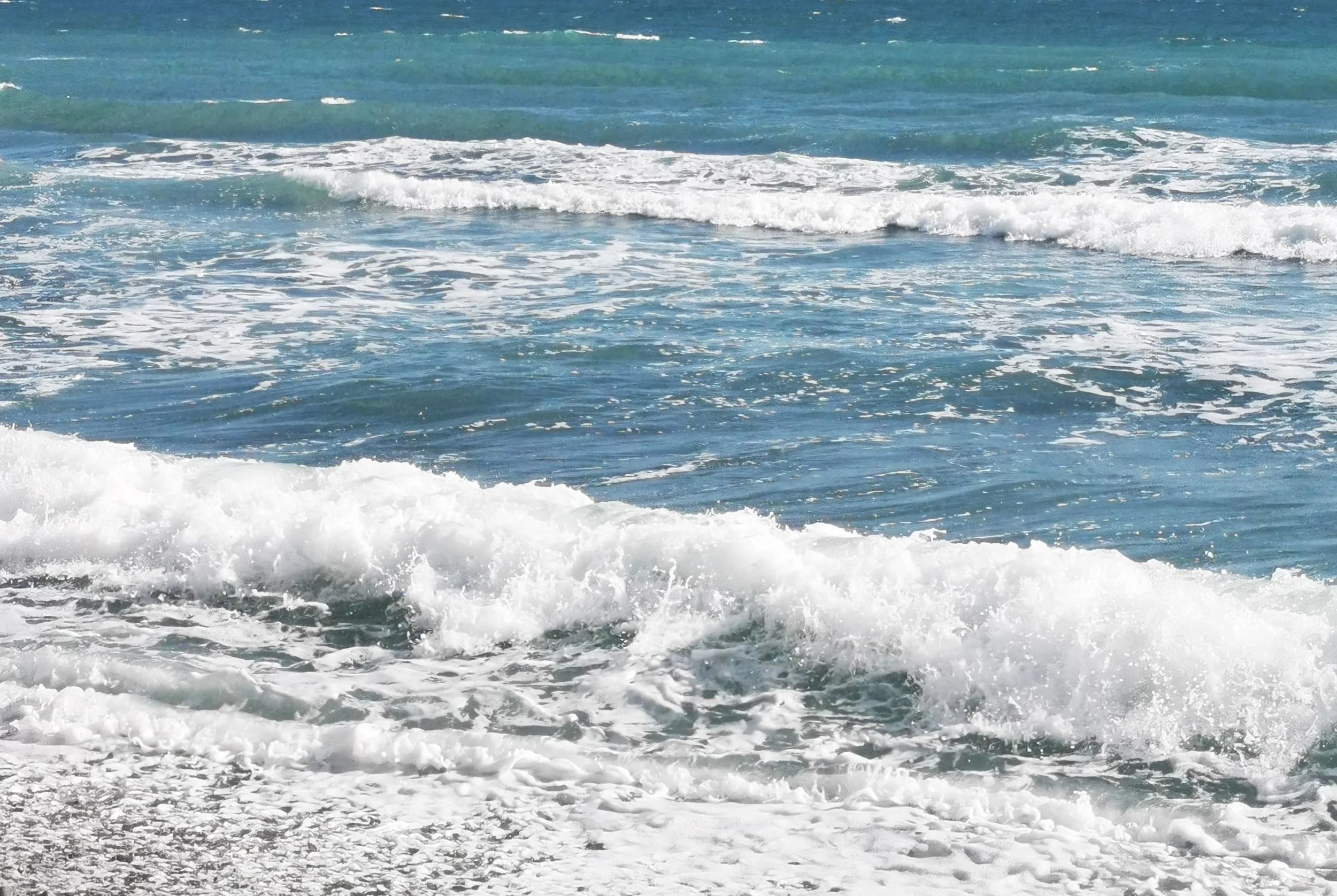 Ocean waves crashing onto the shore with white foam, blue water under a clear sky.