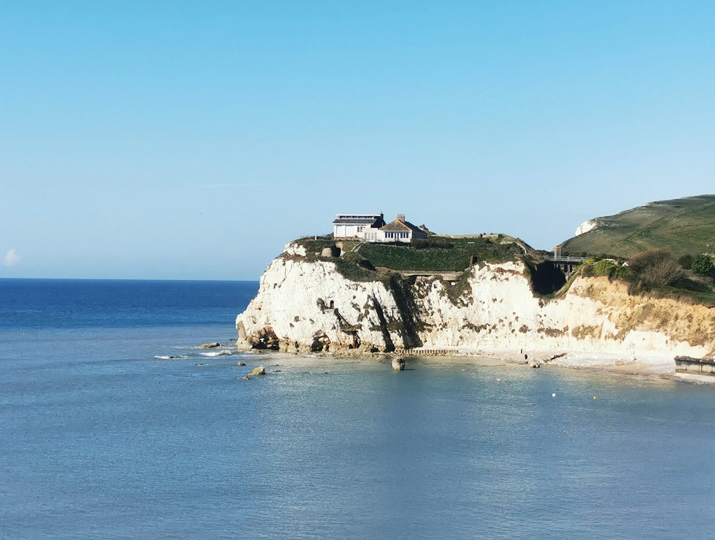 A house on a rocky cliff overlooking the ocean under a blue sky.