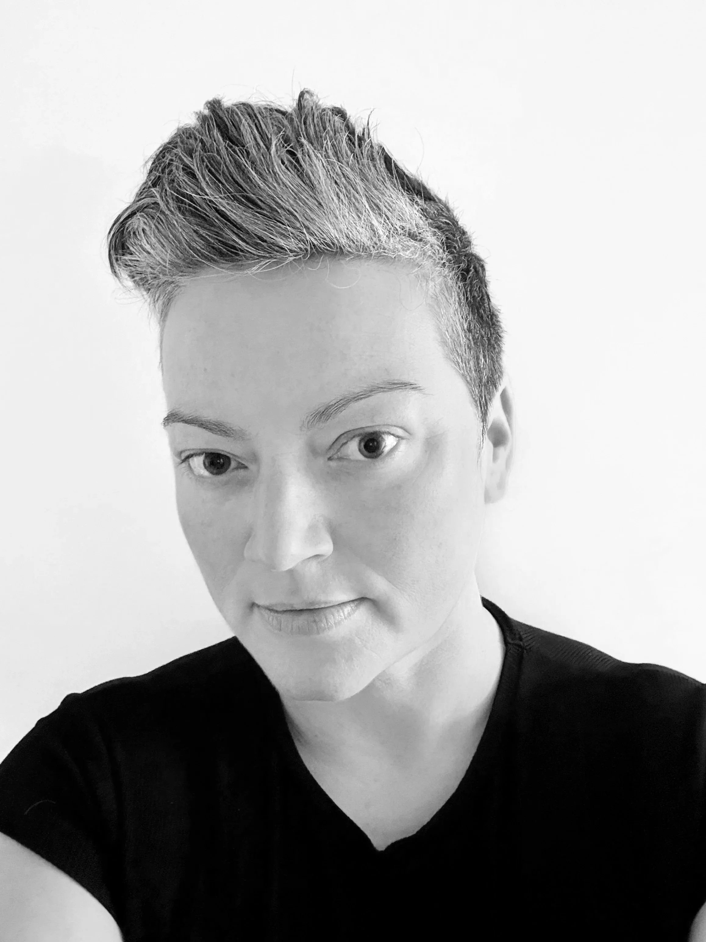 A black-and-white photo of a woman with short hair, wearing a dark top, against a plain light background.