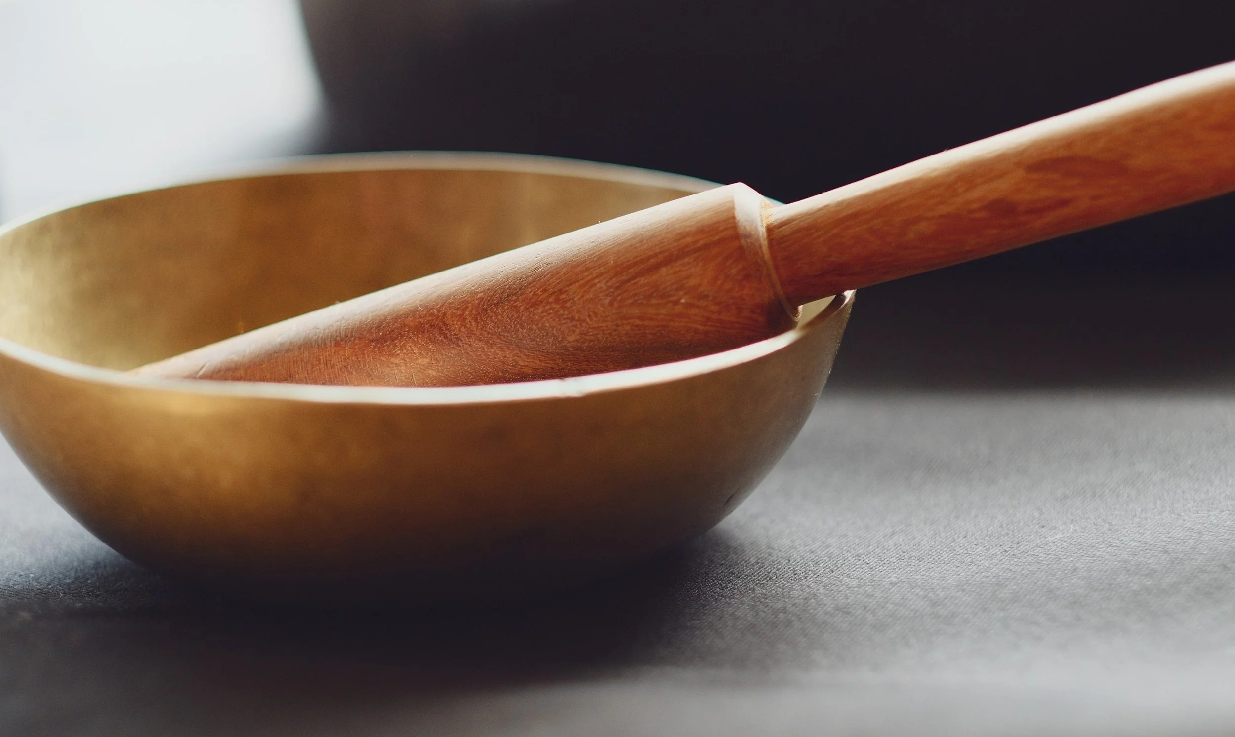 A wooden bowl with a wooden spoon resting inside it, set on a dark surface.