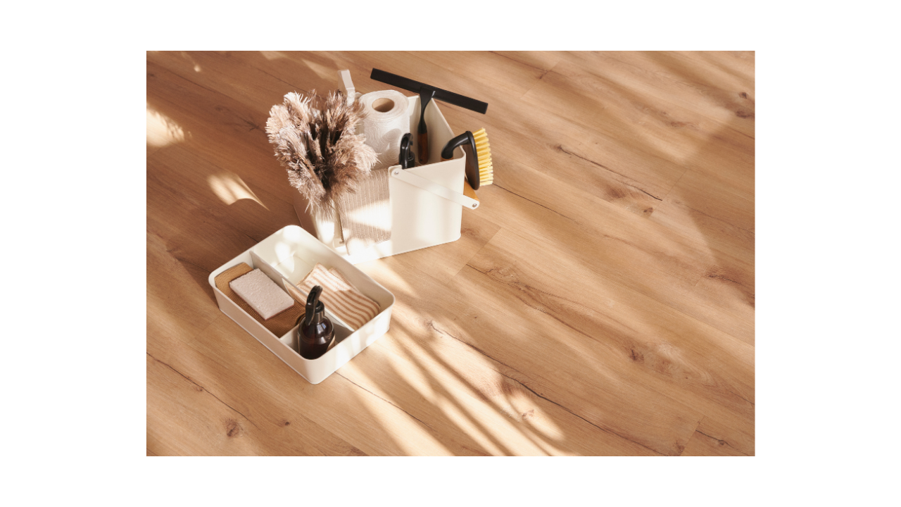 Cleaning supplies arranged on a wooden floor, including brushes, a spray bottle, and sponges in containers.