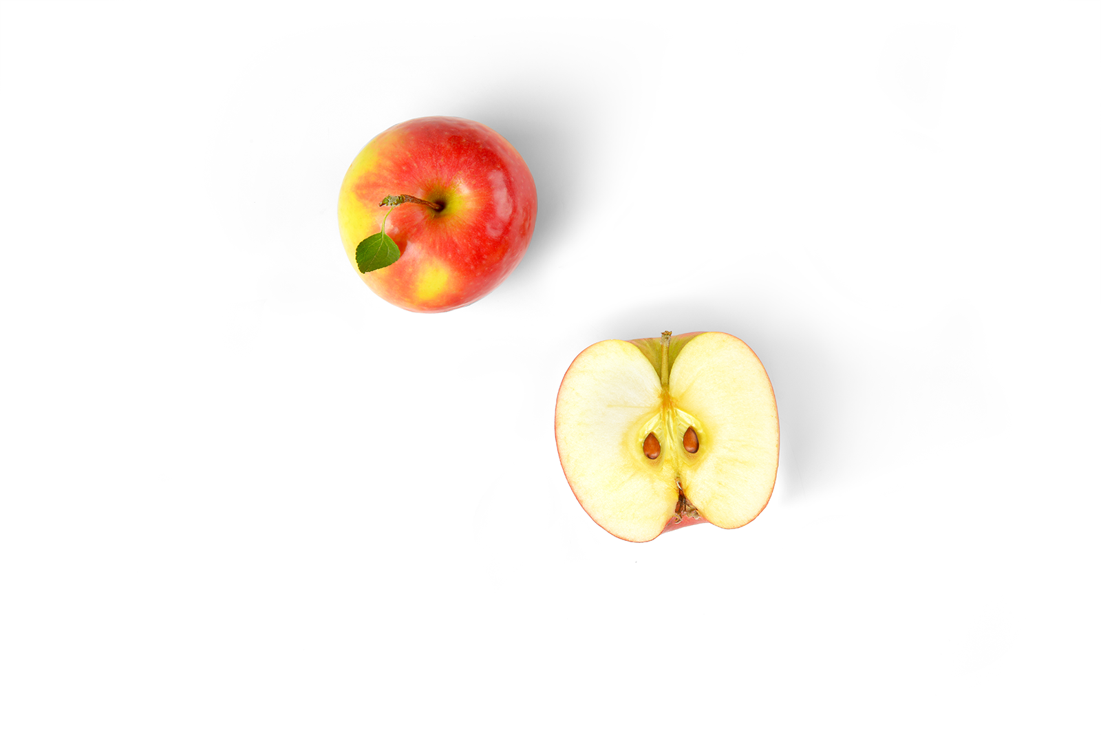 Whole red and yellow apple with a leaf and a sliced half showing the seeds inside.