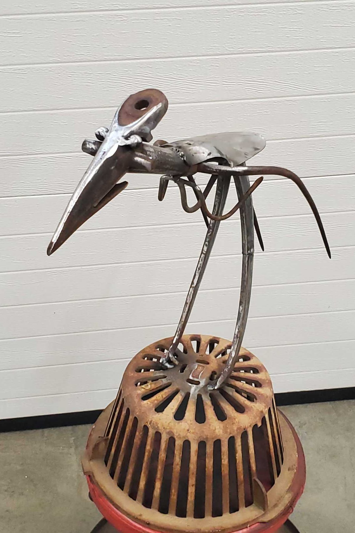 A sculpture made from scrap metal resembling a bird standing on a rusted, circular metal base.