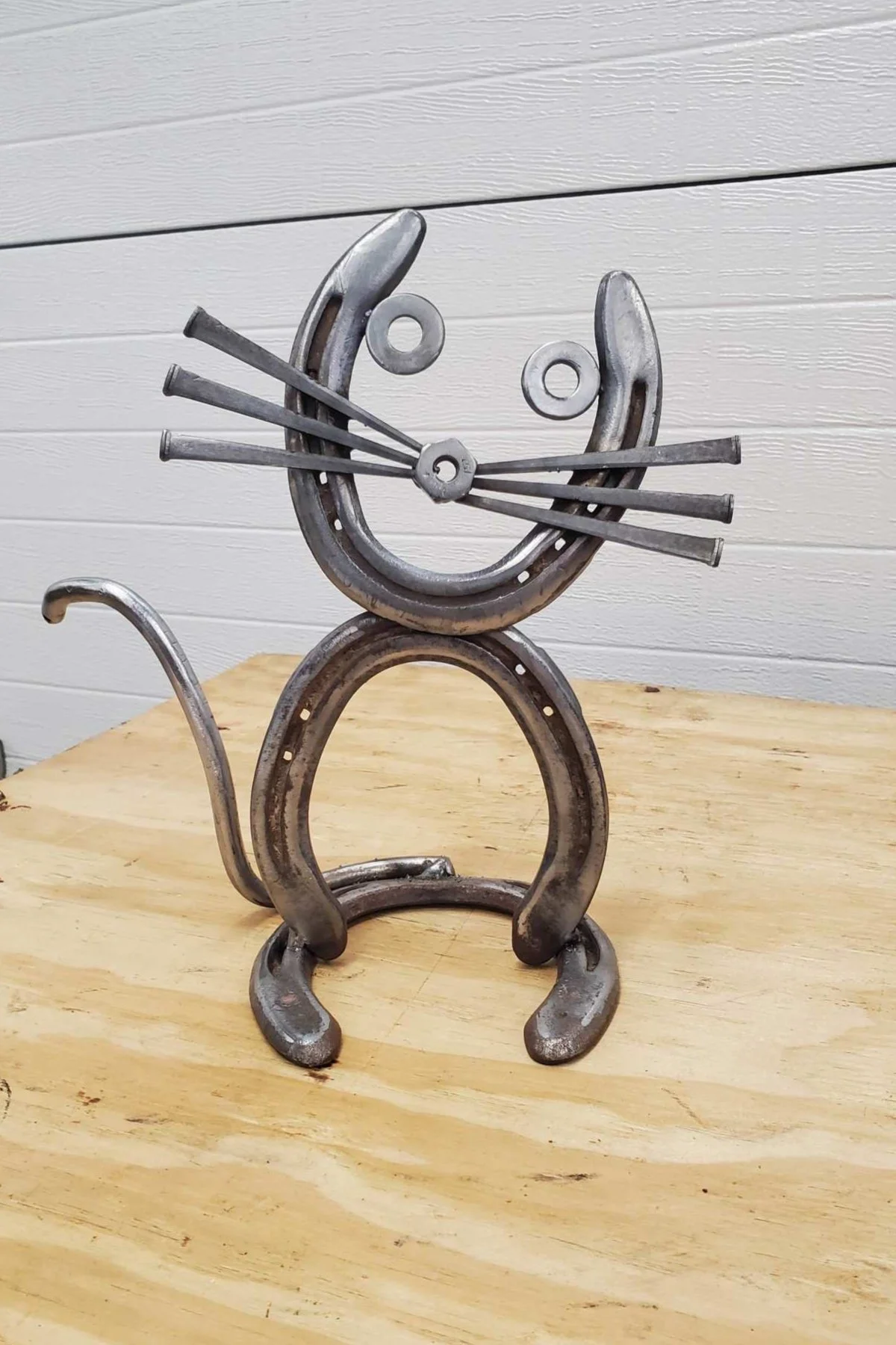 Metal sculpture resembling a smiling cat with whiskers and a tail, set on a wooden surface.