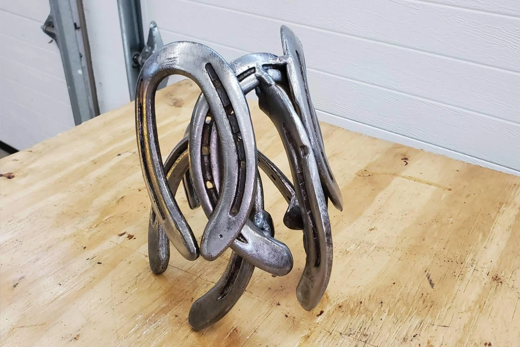 A pile of metal horse shoes stacked on a wooden surface in a workshop setting.