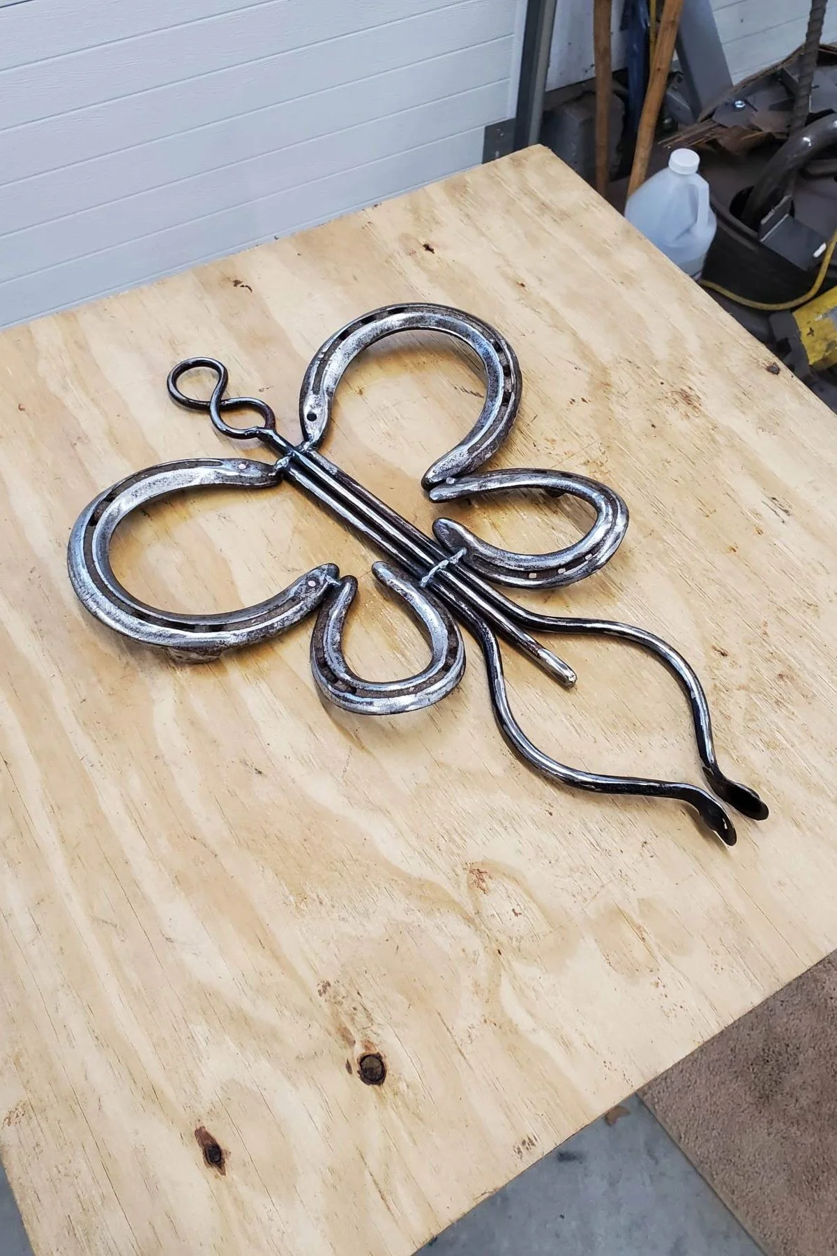 Metal decorative butterfly shaped piece with scrollwork, placed on a wooden workbench in a workshop.
