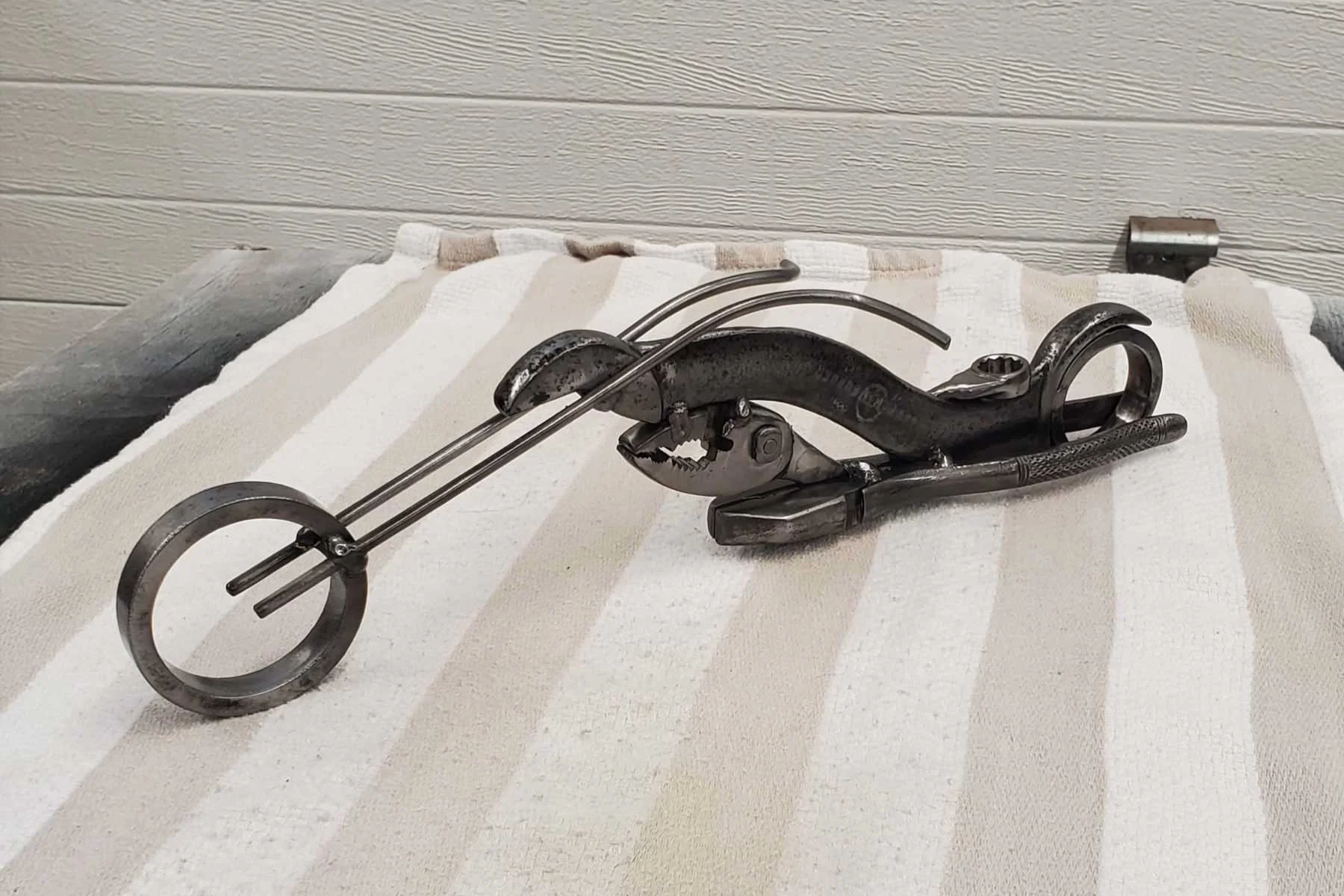 Metal sculpture of a motorcycle made from scrap car parts on a striped towel.