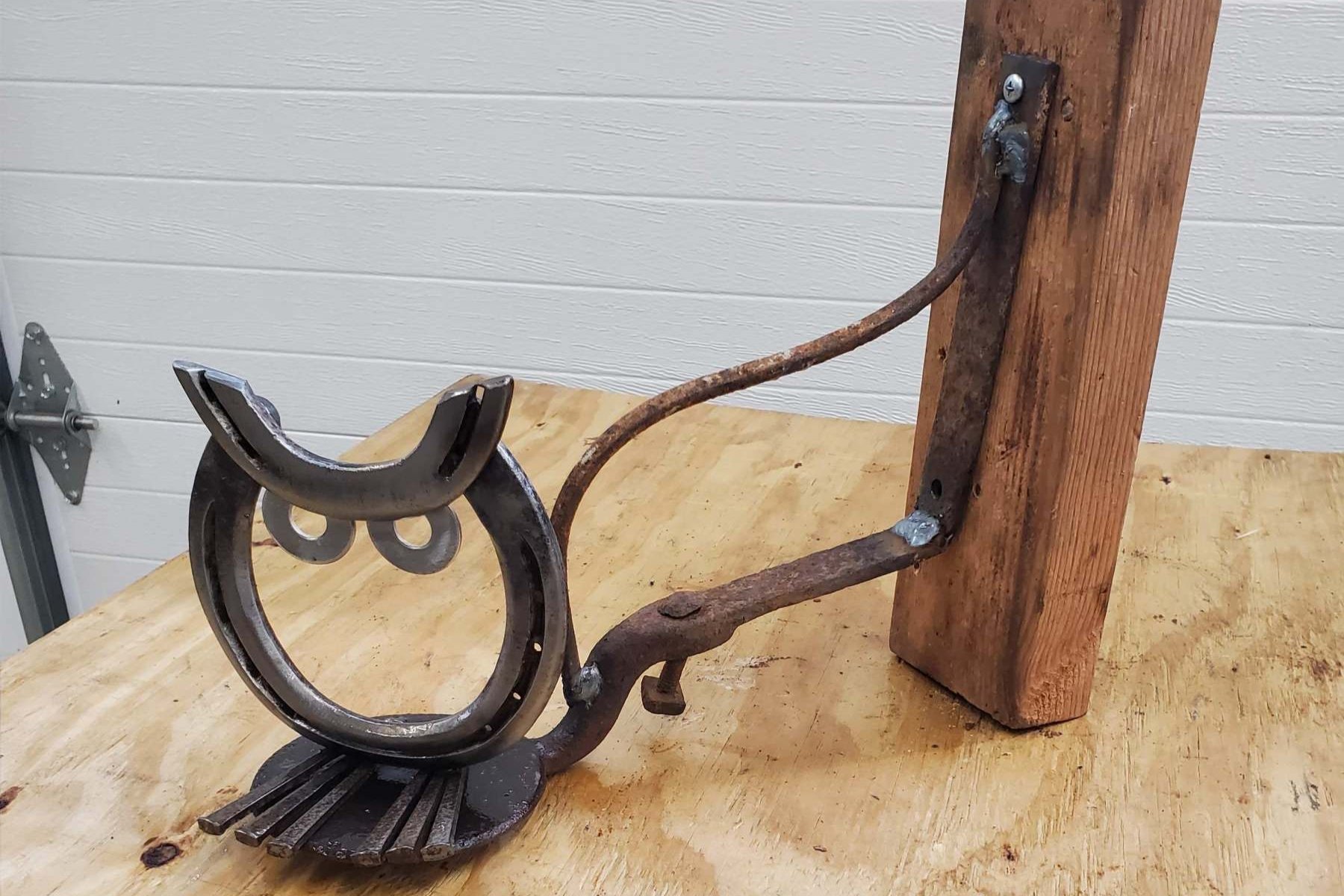 A homemade owl sculpture made from a horseshoe, metal, wood, and metal screws, attached to a wooden post.