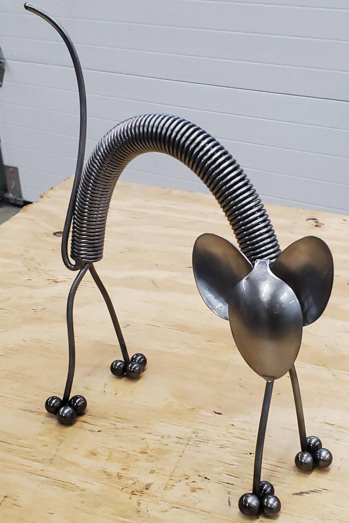 A metal sculpture of a dog with a spring neck, ball feet, and large ears, on a wooden surface.