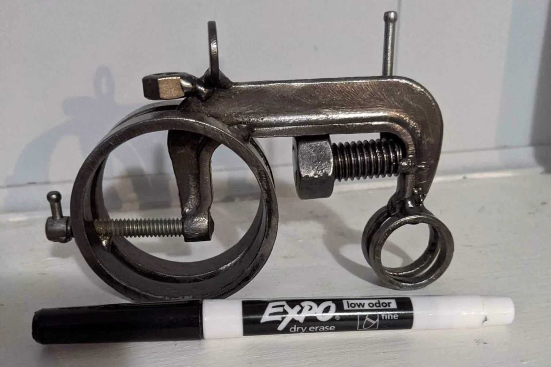 A metal sculpture of a tractor from a circular opening, a threaded bolt, and a smaller ring attached to a chain, placed on a white surface, 