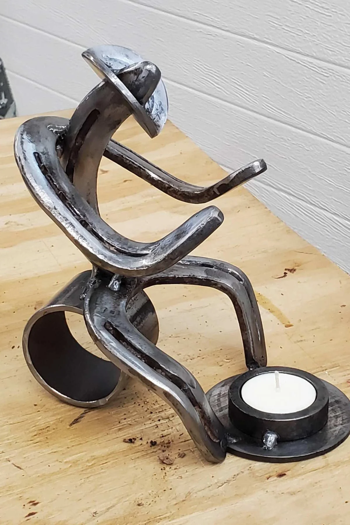 A decorative sculpture made from bent metal strips resembling a person riding a scooter, with a tea light candle holder at the base.