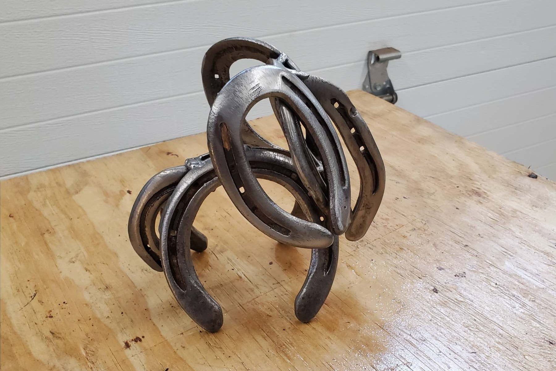 A sculpture made from horse shoes is displayed on a wooden table against a white wall.