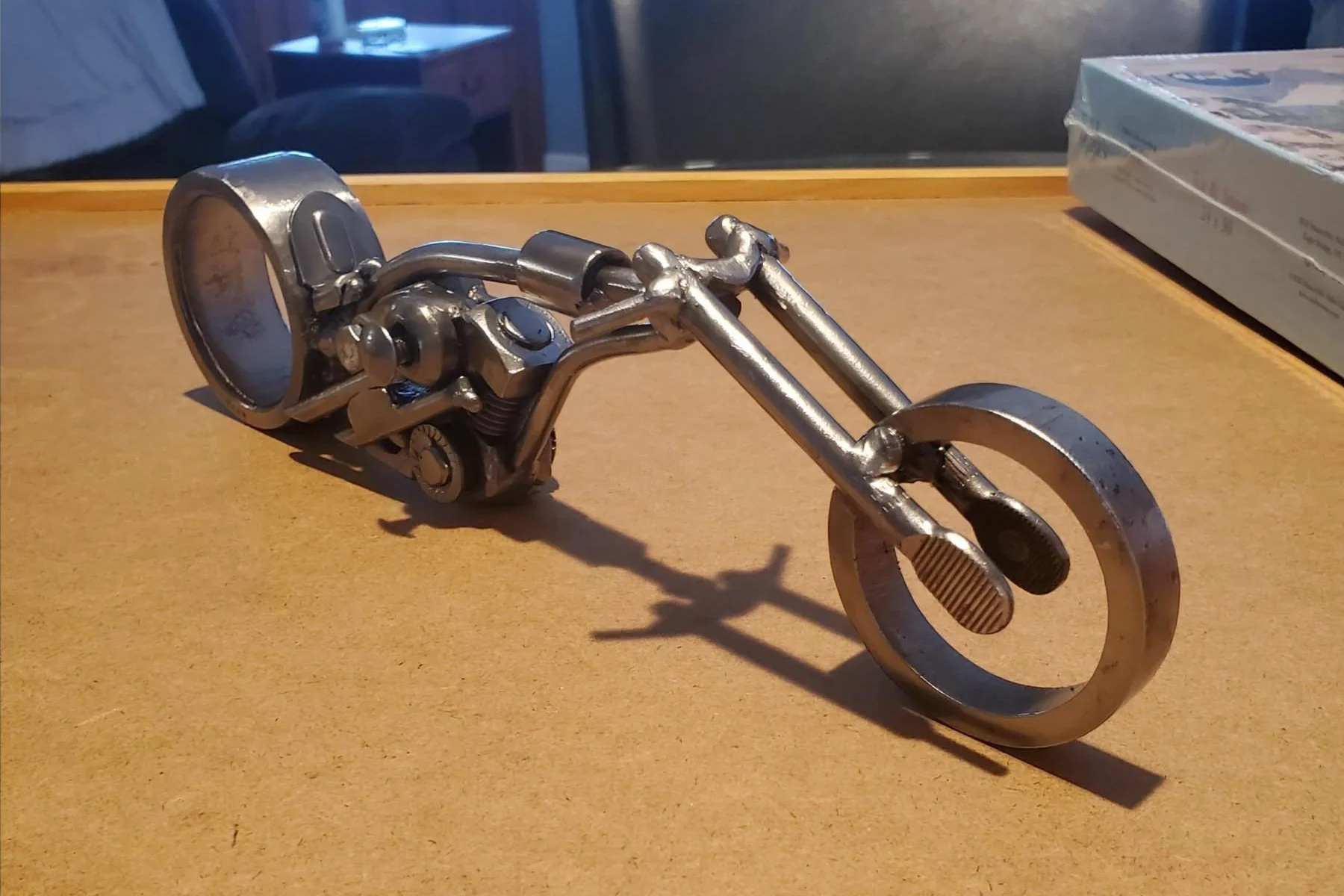 Metal sculpture of a motorcycle on a wooden surface, with a shadow cast behind it.