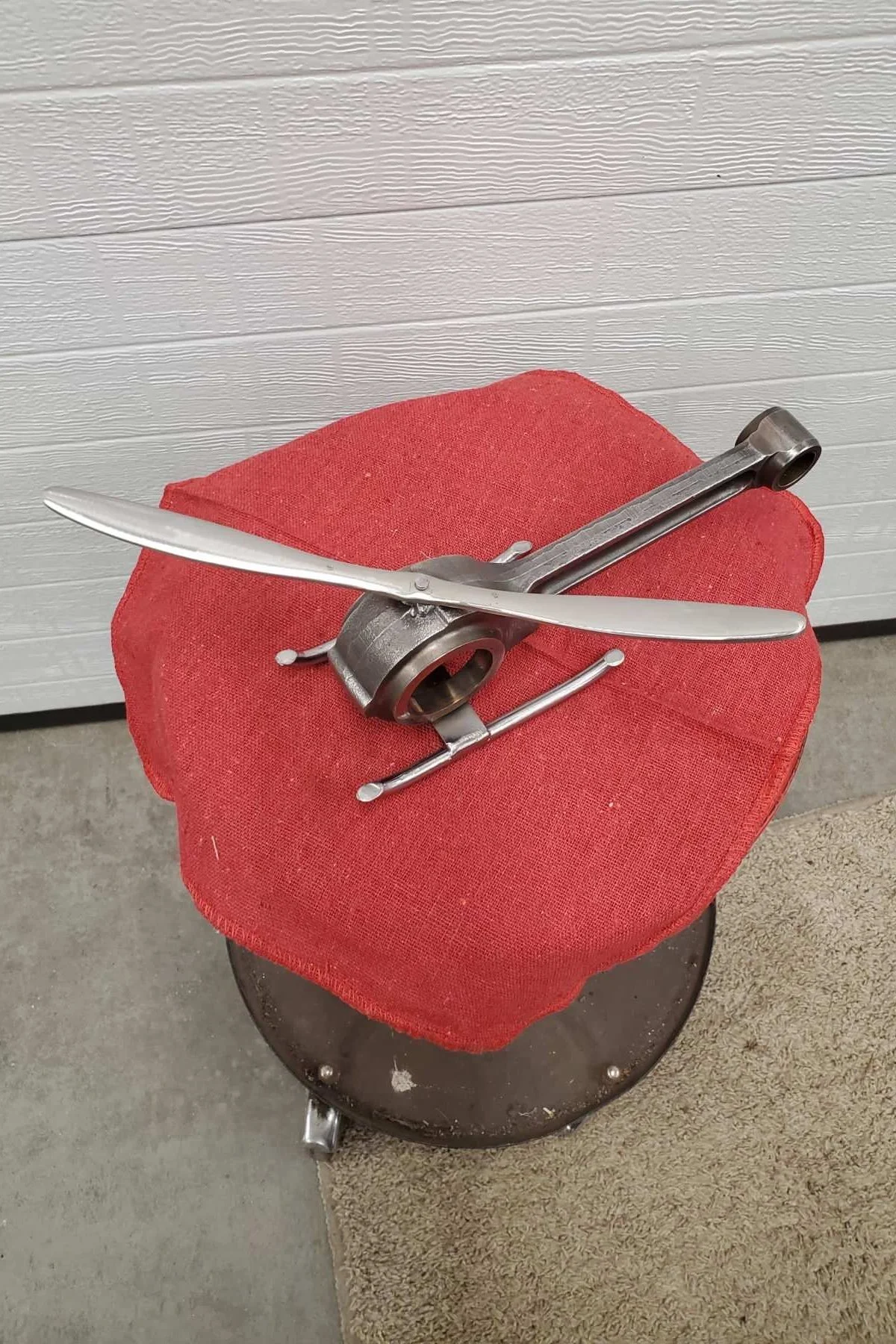 A sculpture made from scrap metal parts resembling a helicopter, mounted on a chair on a red cover