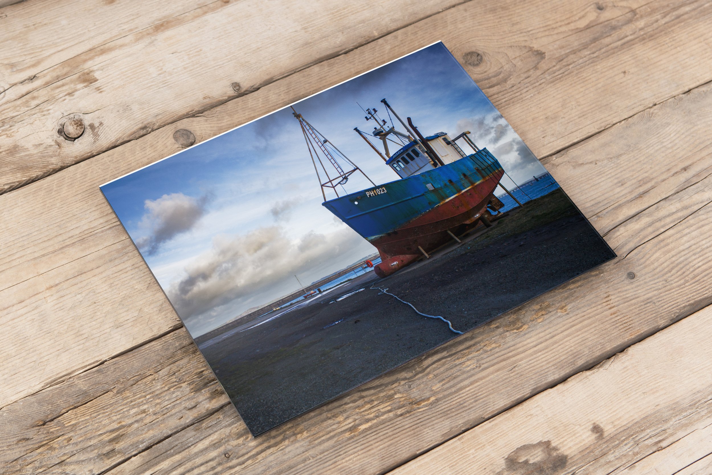 Photograph of an old boat on the shore with cloudy sky in the background.