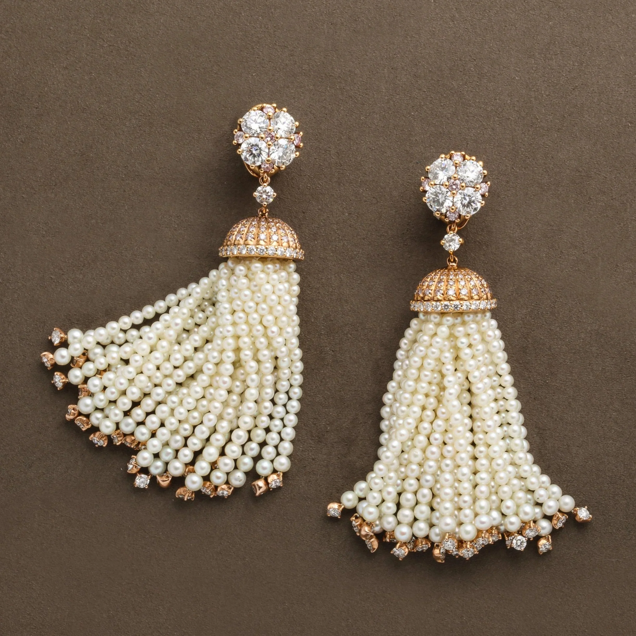 Pair of pearl, pink diamonds, white diamond, and gemstone earrings with floral top design, gold accents, and hanging pearl tassels on a brown background.