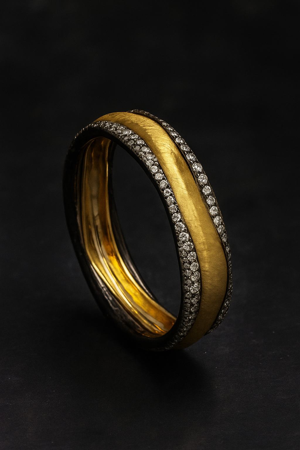 A close-up of an 18k yellow gold and diamond bangle by Donna Vock, decorated with small diamonds along the edges, set against a black background.