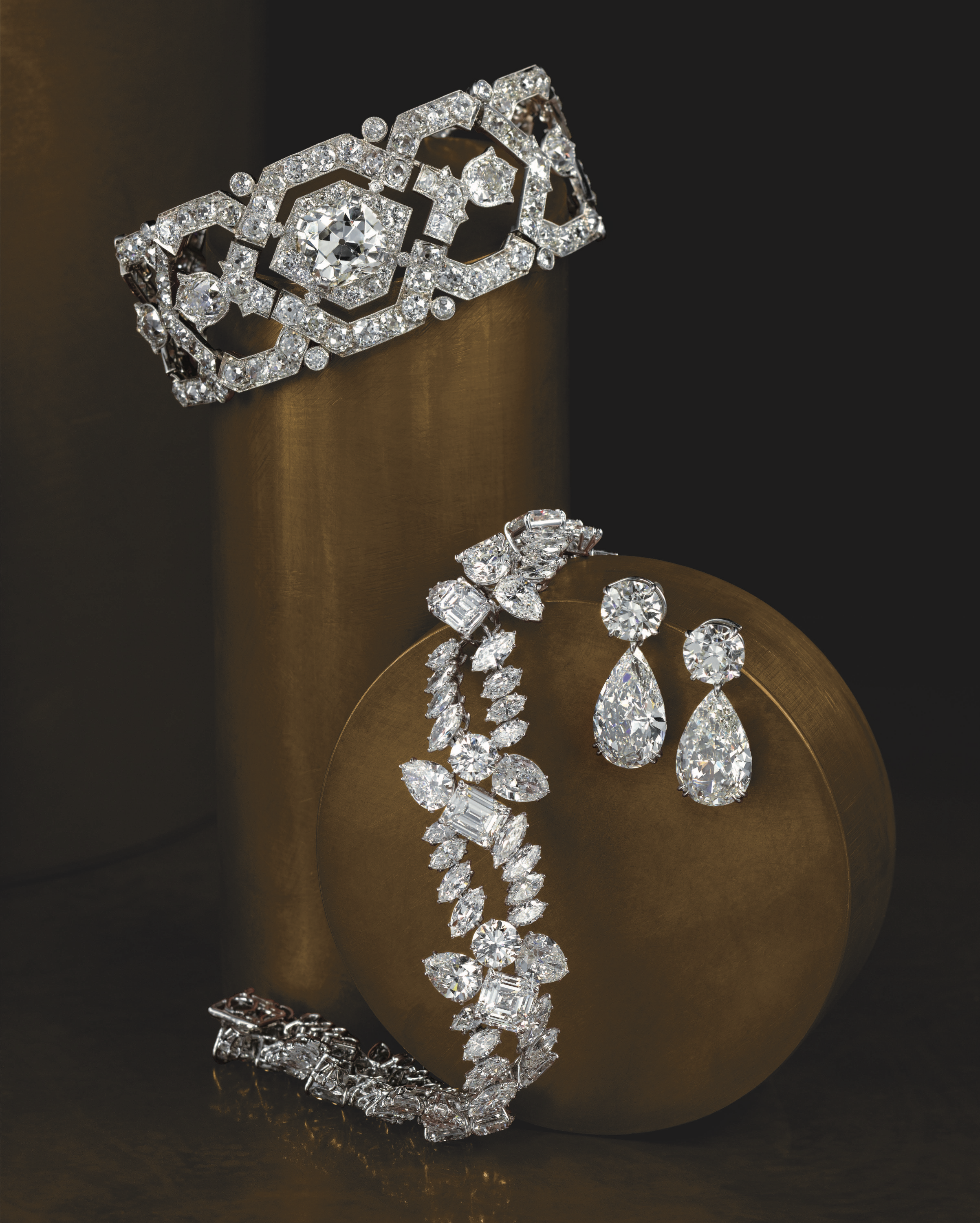 A collection of vintage collectible diamond jewelry, including a bracelet, earrings, and a necklace, displayed on a golden cylindrical stand with a black background.