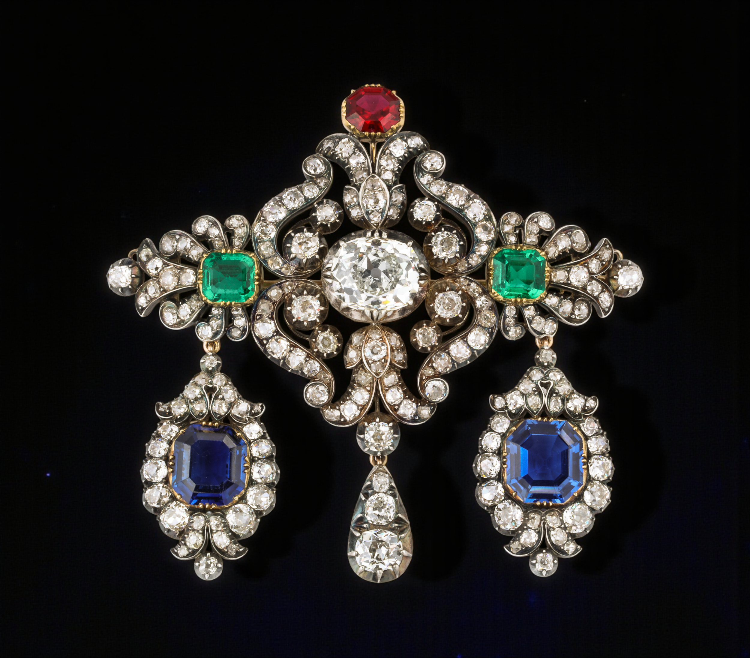 Devant De Corsage vintage brooch with diamonds, blue sapphire, green emerald, red rubies, all set against a black background.