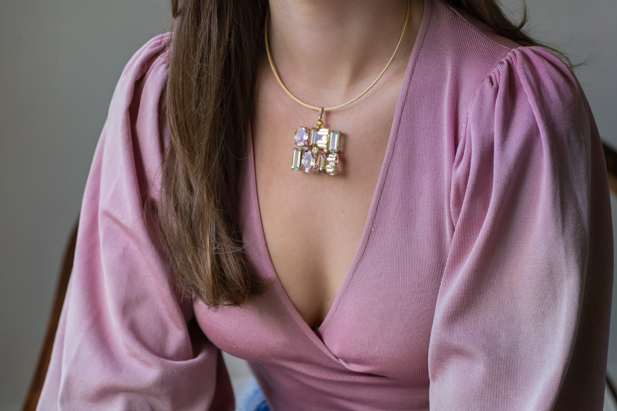 Custom Donna Vock Necklace. Close-up of a woman wearing a pink top and an 18k yellow gold necklace with a large, colorful gemstone pendant.