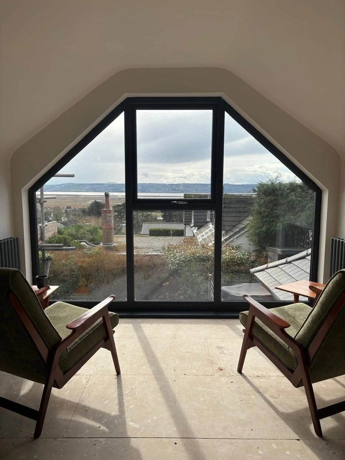 Interior of a room with two green armchairs facing a large, unique bespoke window project with a scenic view of houses