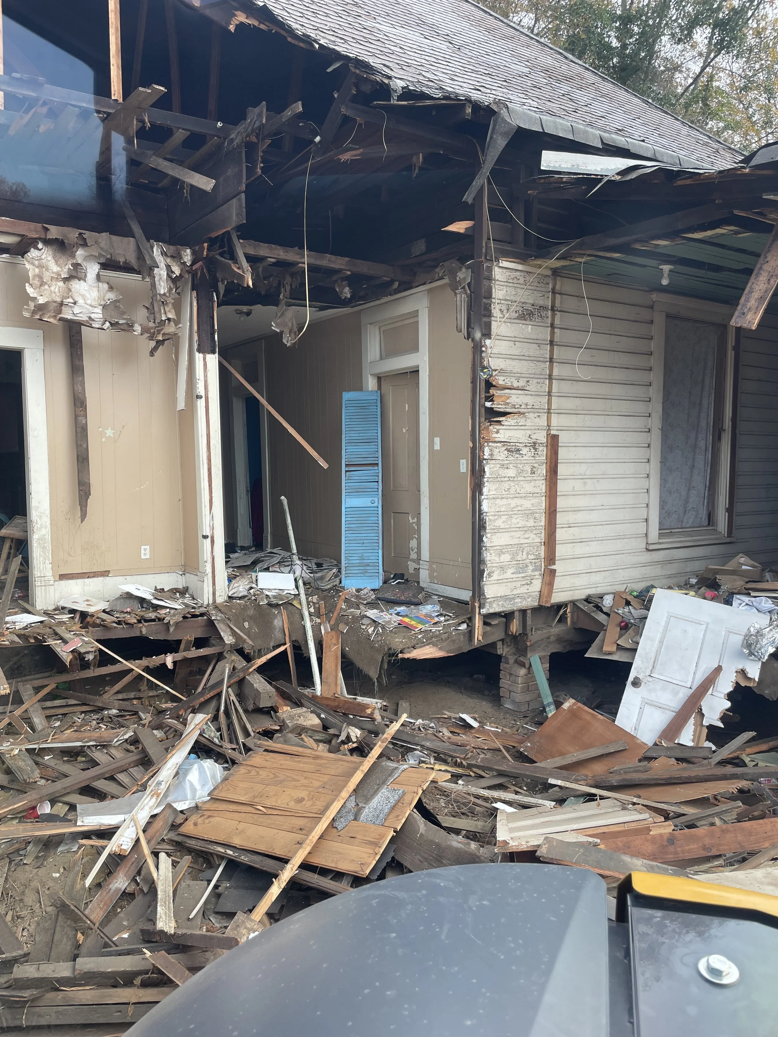 A house being demloished with parts of the roof and walls collapsed, debris scattered around, and a door tilted inward.