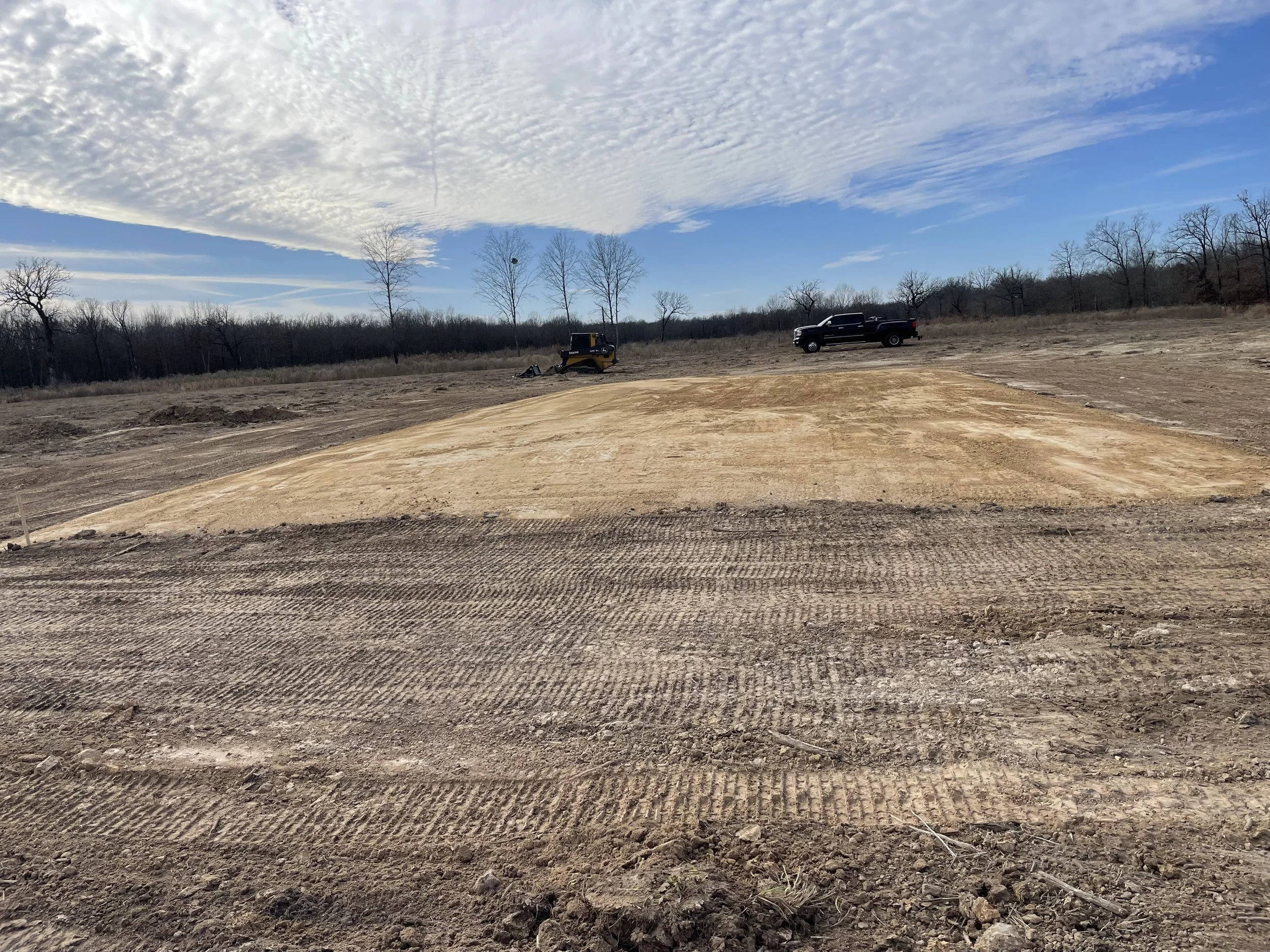 Construction site with cleared and leveled land, construction equipment, a pickup truck, and a blue sky with clouds.