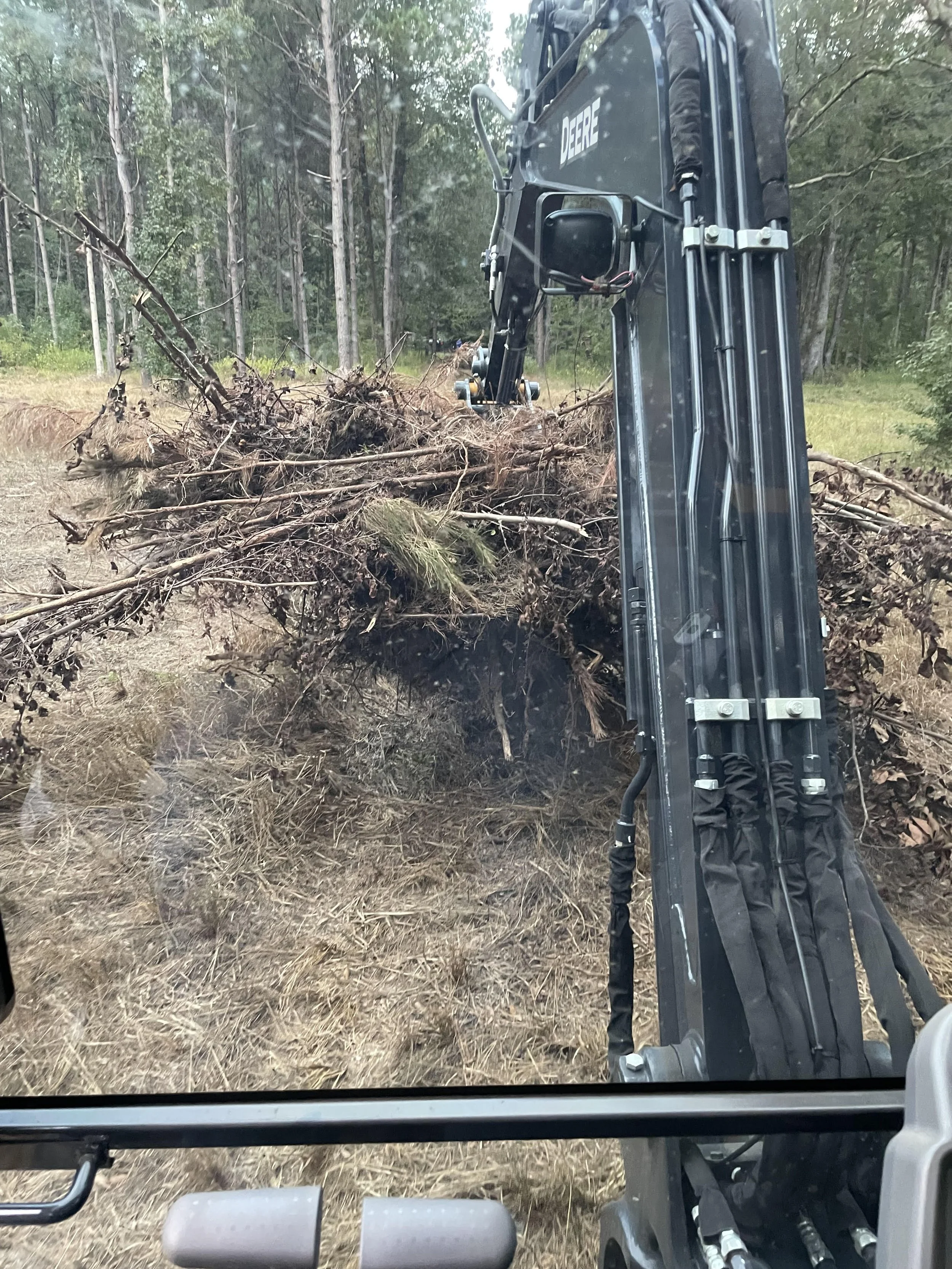 View from inside a vehicle with a mechanical arm clearing fallen trees and branches in a wooded area.