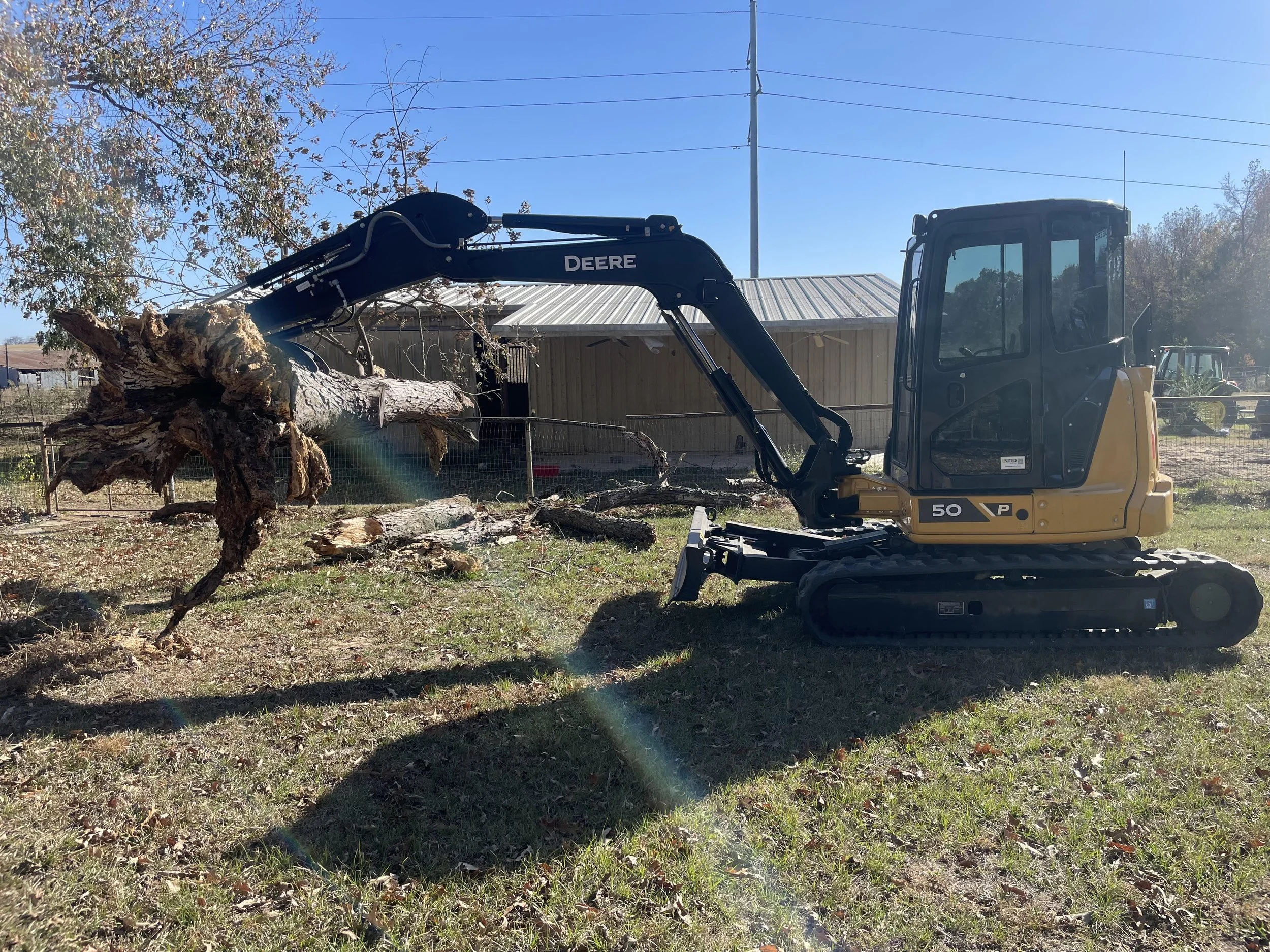 A yellow John Deere compact excavator lifting a large fallen tree. 