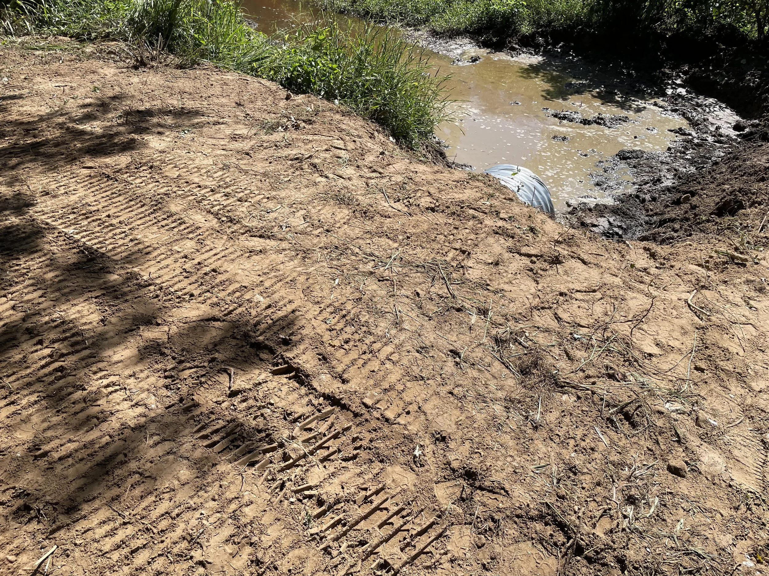 Excavated dirt bank with tire tracks and a newly installed culvert underneath.