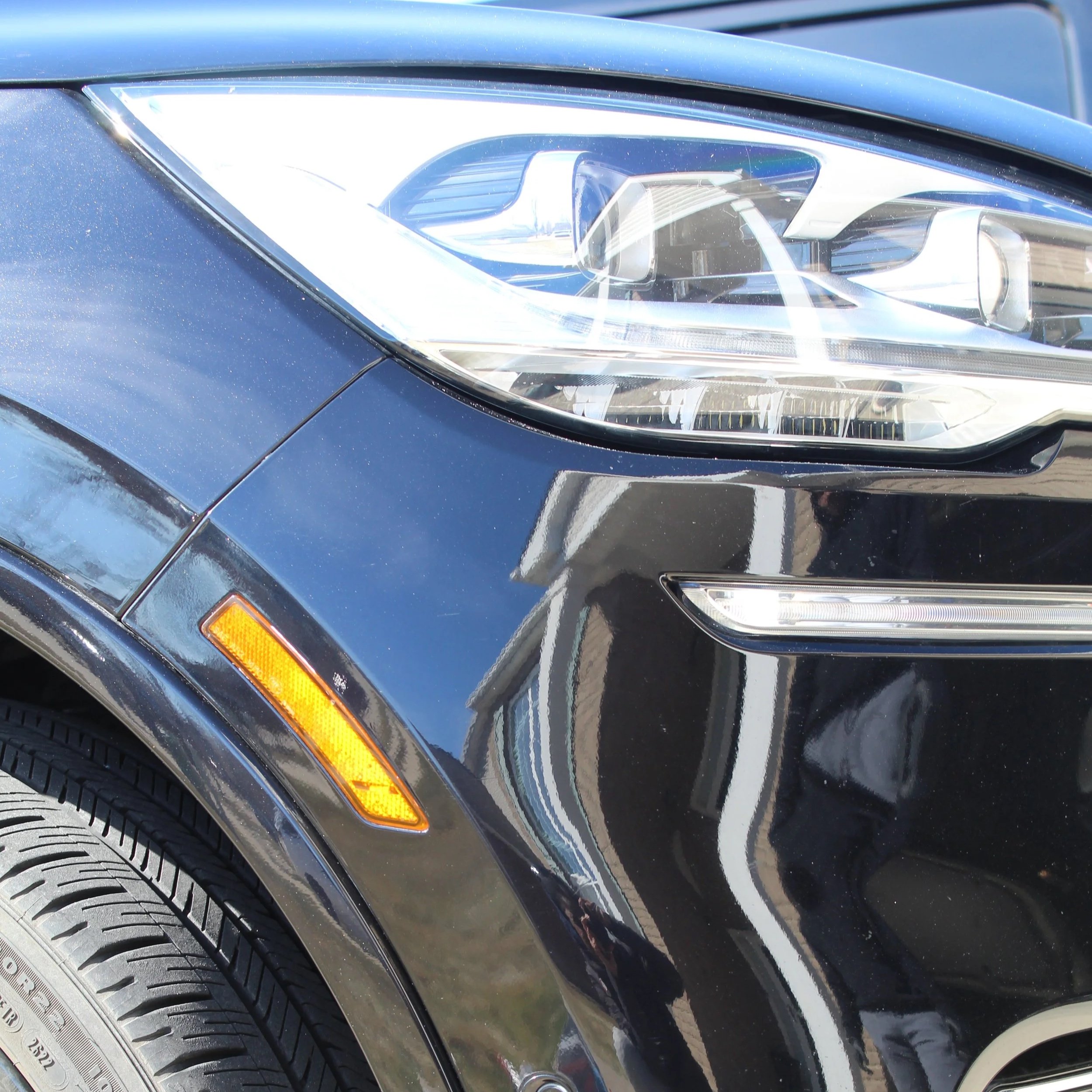 Close-up of a car's headlight and tire, showing part of the front of the car with a glossy blue finish.