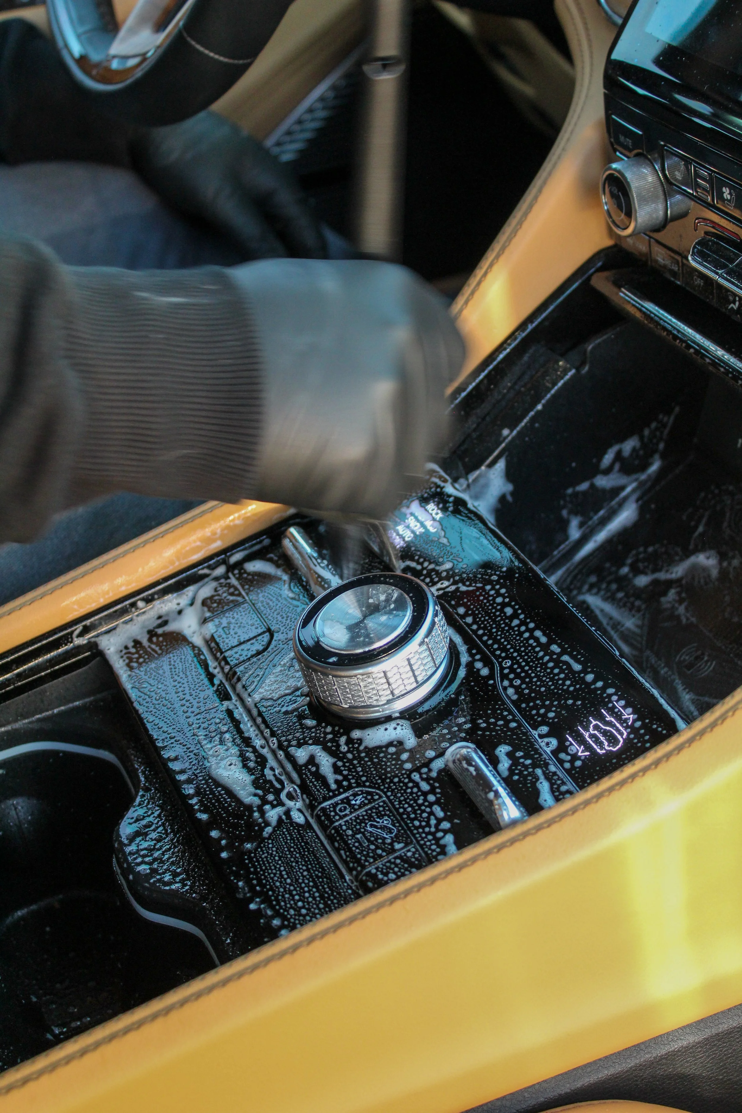 Person cleaning the center console of a yellow car with soap and water, showing a digital display and control knob.