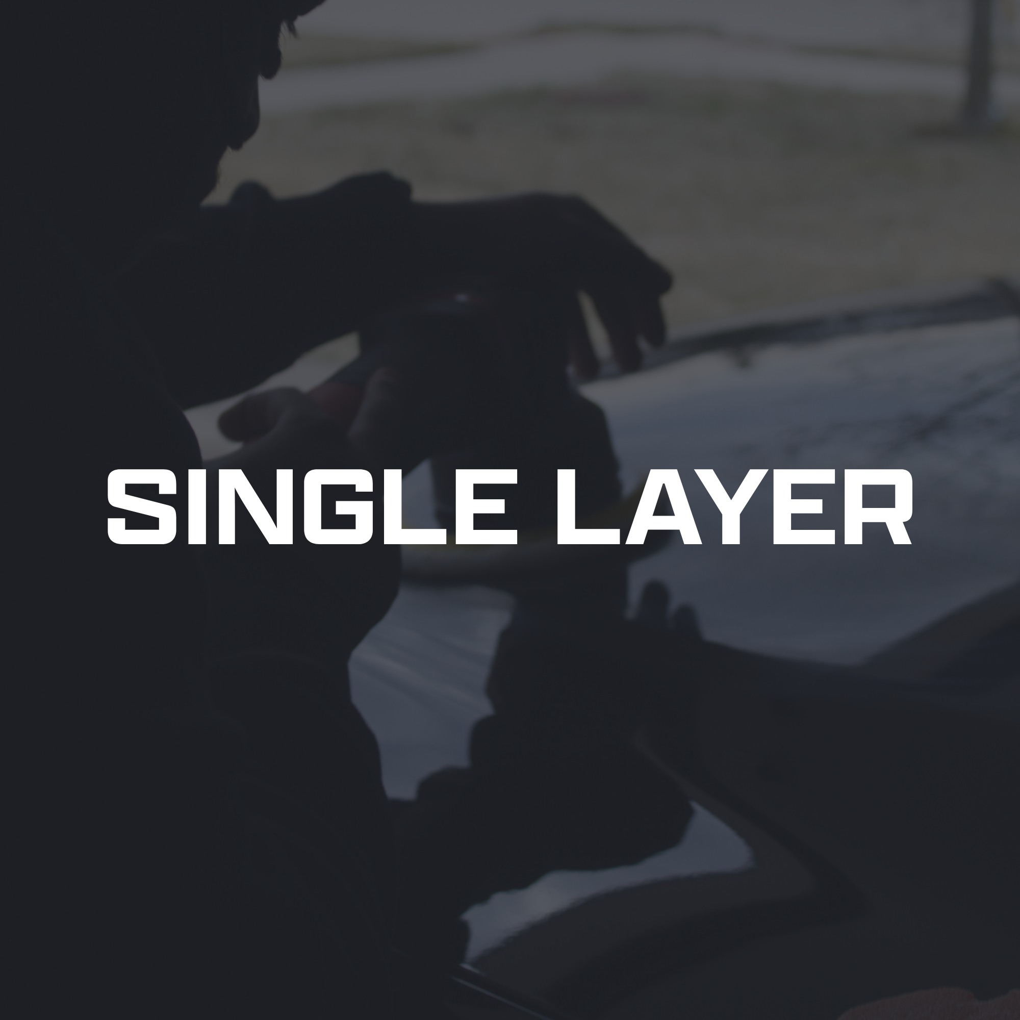 Silhouette of a person with a cap, sitting outdoors and looking down, with a blurred background and overlaying white text that reads "SINGLE LAYER."