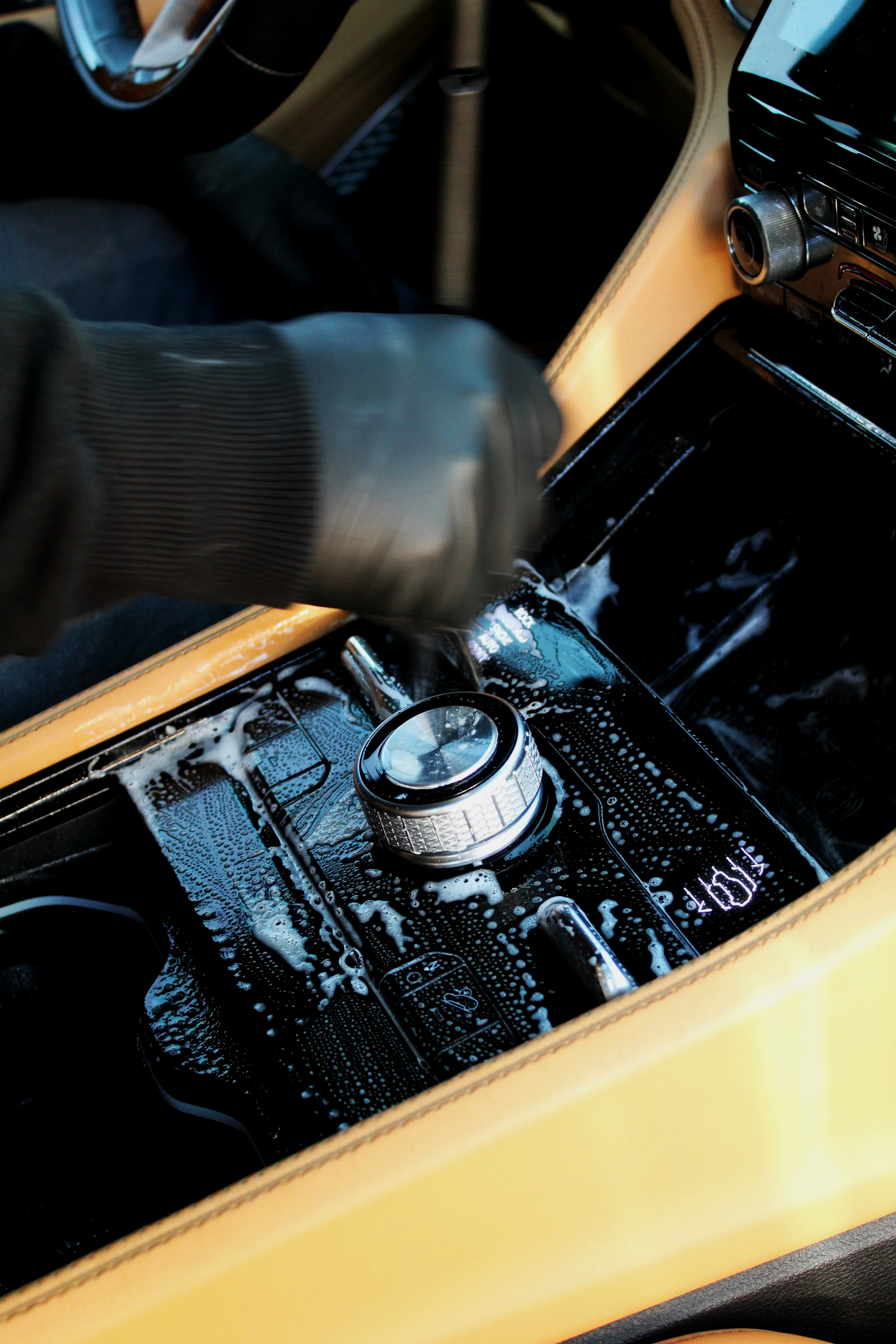 Man using brush and soap to do an interior detail of the center console of a Jeep Grand Cherokee. 