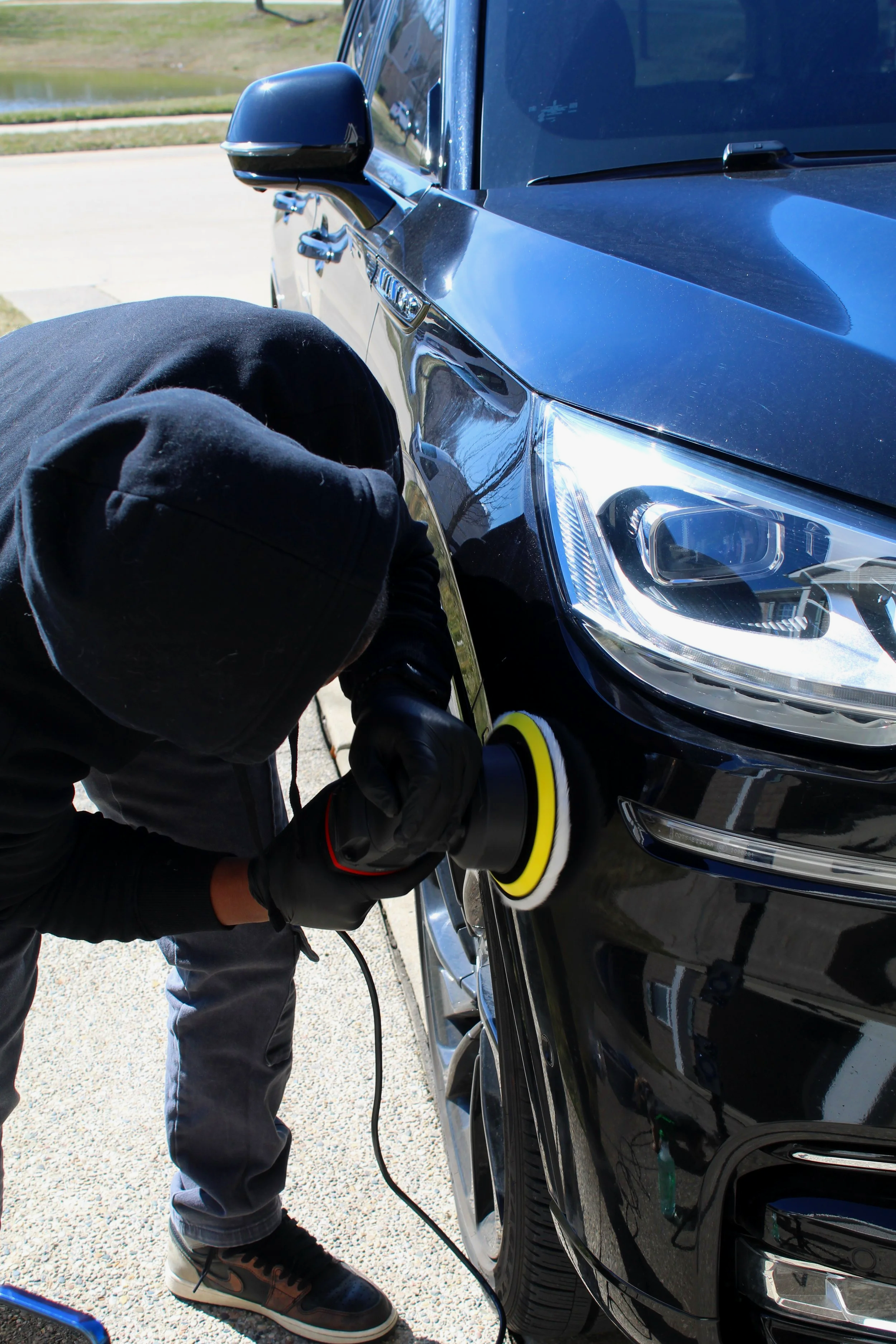 Man using a orbital machine to remove scratches from car paint on a Lincoln Aviator.