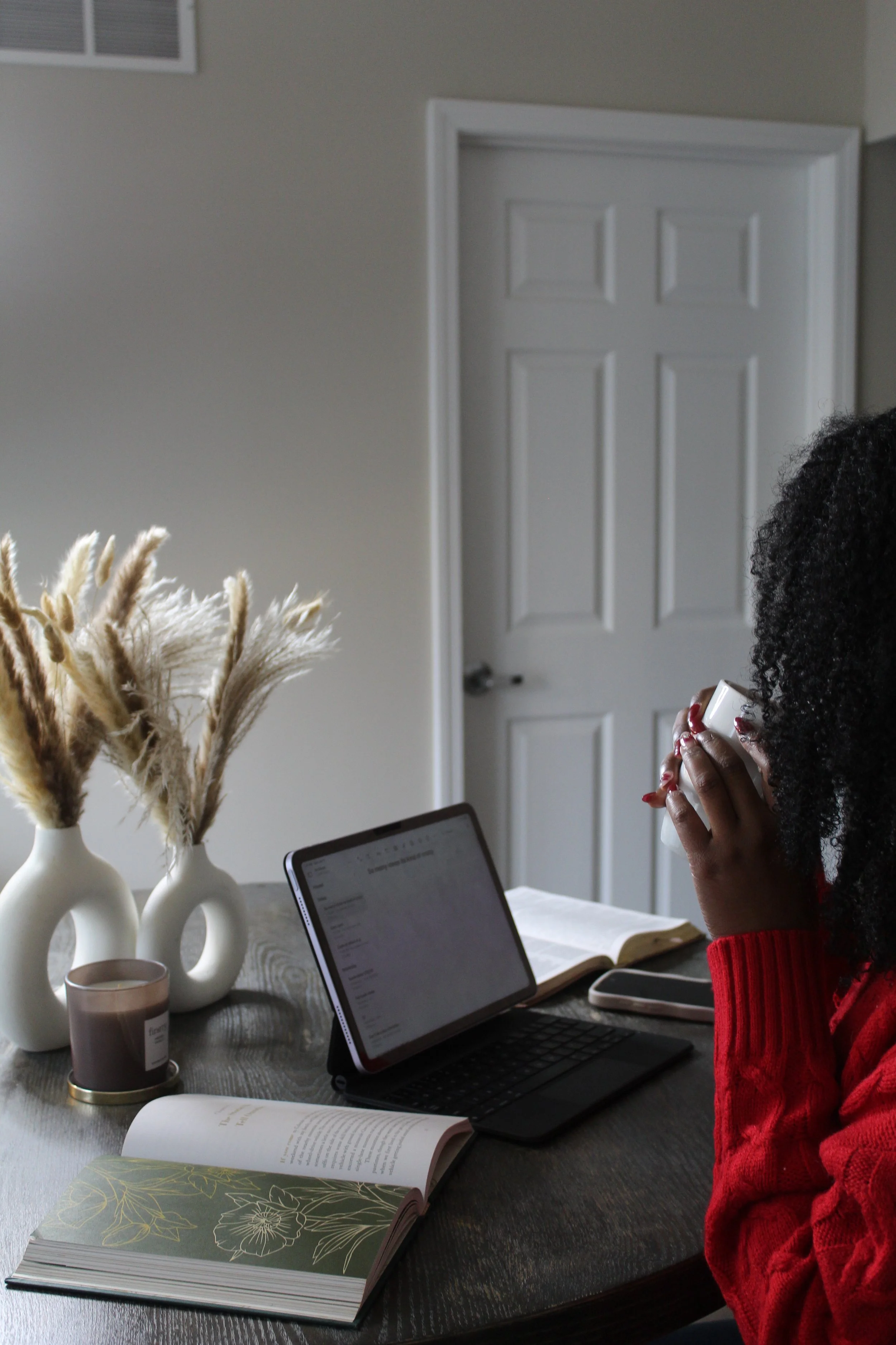 Black girl/woman holding a cup full of tea. modern vase with flowers. iPad with keyboard open to notes app. Devotional book open. vanilla candle. iPhone 16. Holy bible