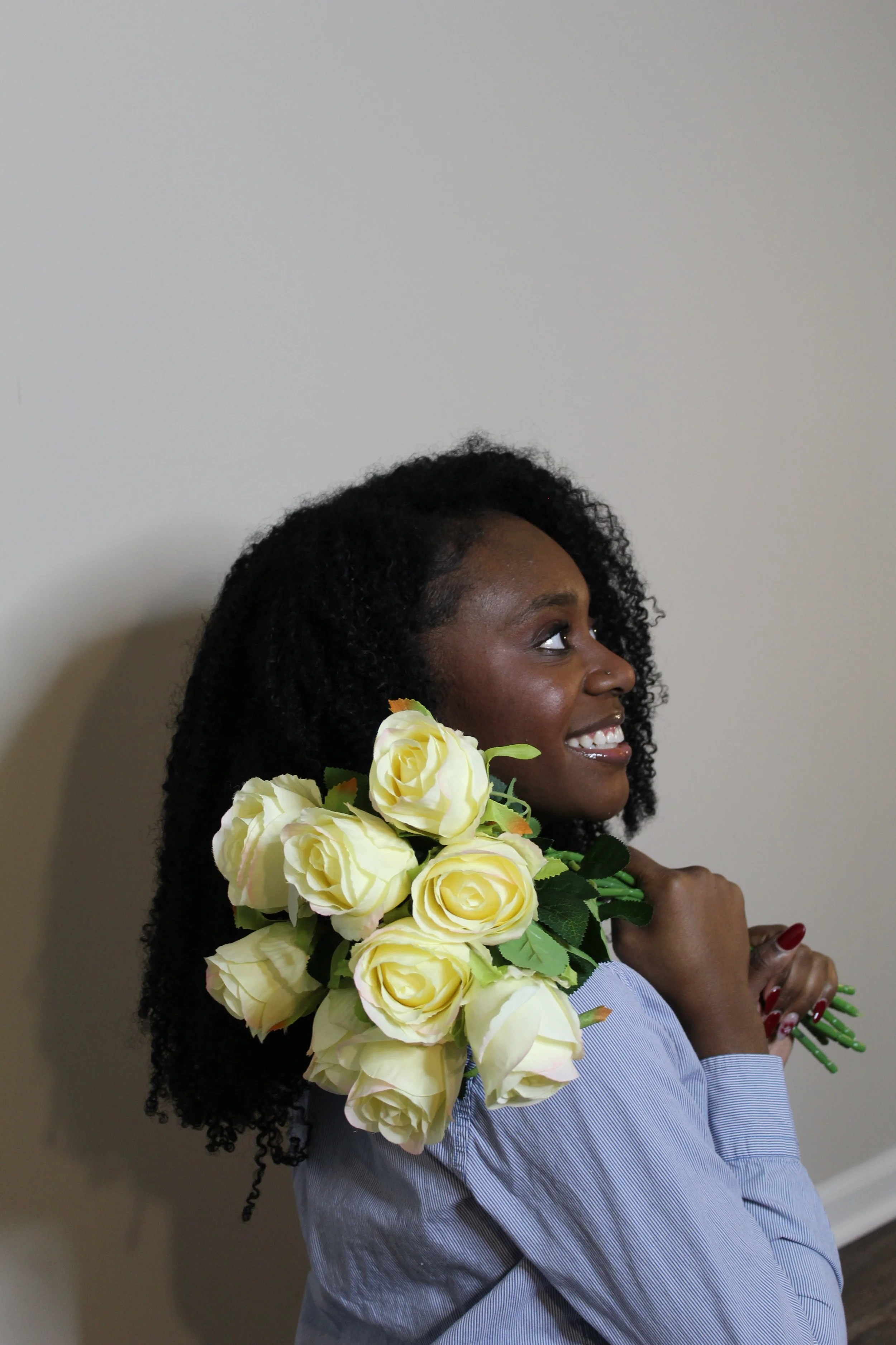 A smiling woman with dark curly hair holding a bouquet of white roses.
