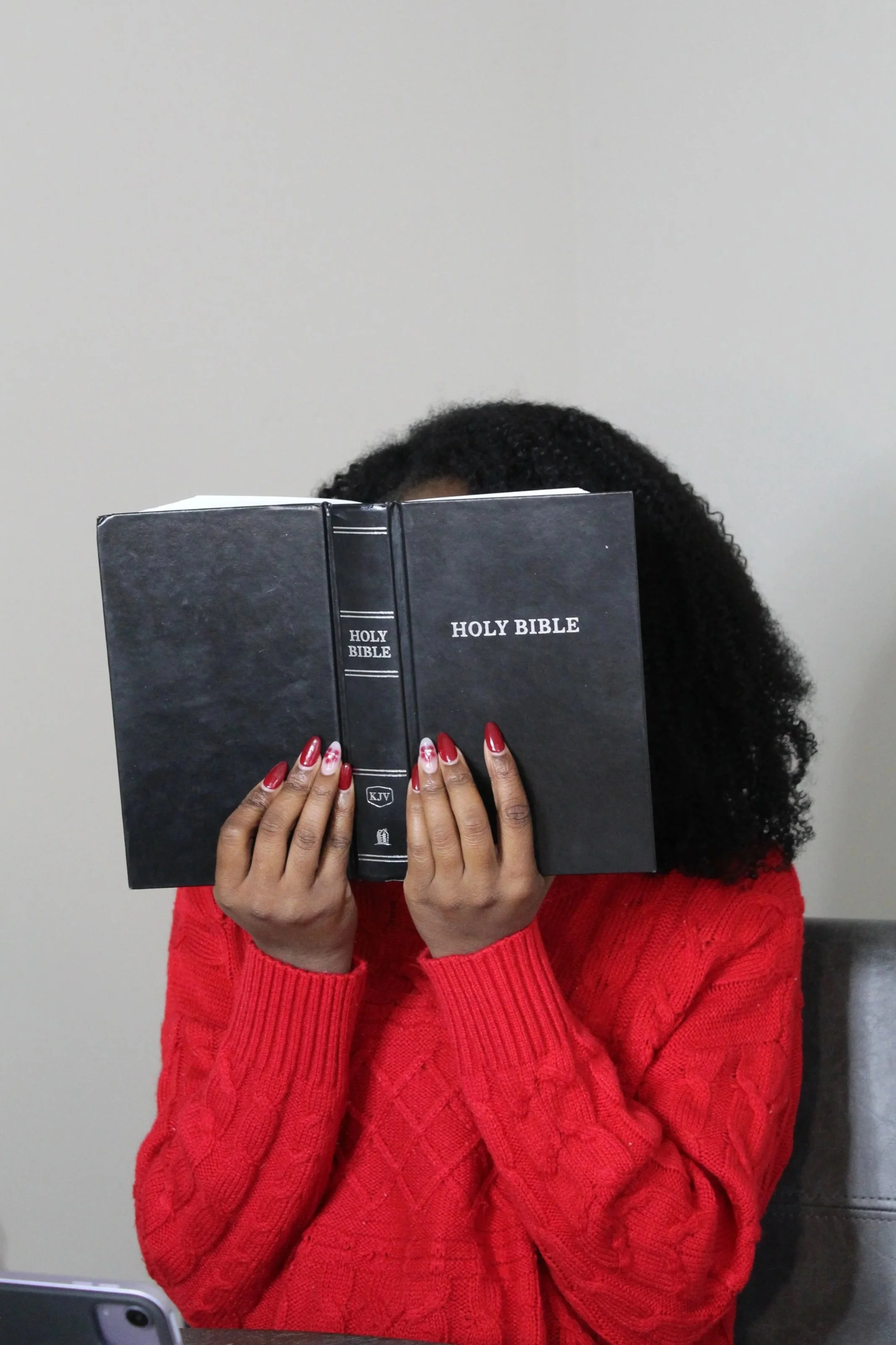 Girl holding a Holy Bible in a red sweater and red acrylic nails.
