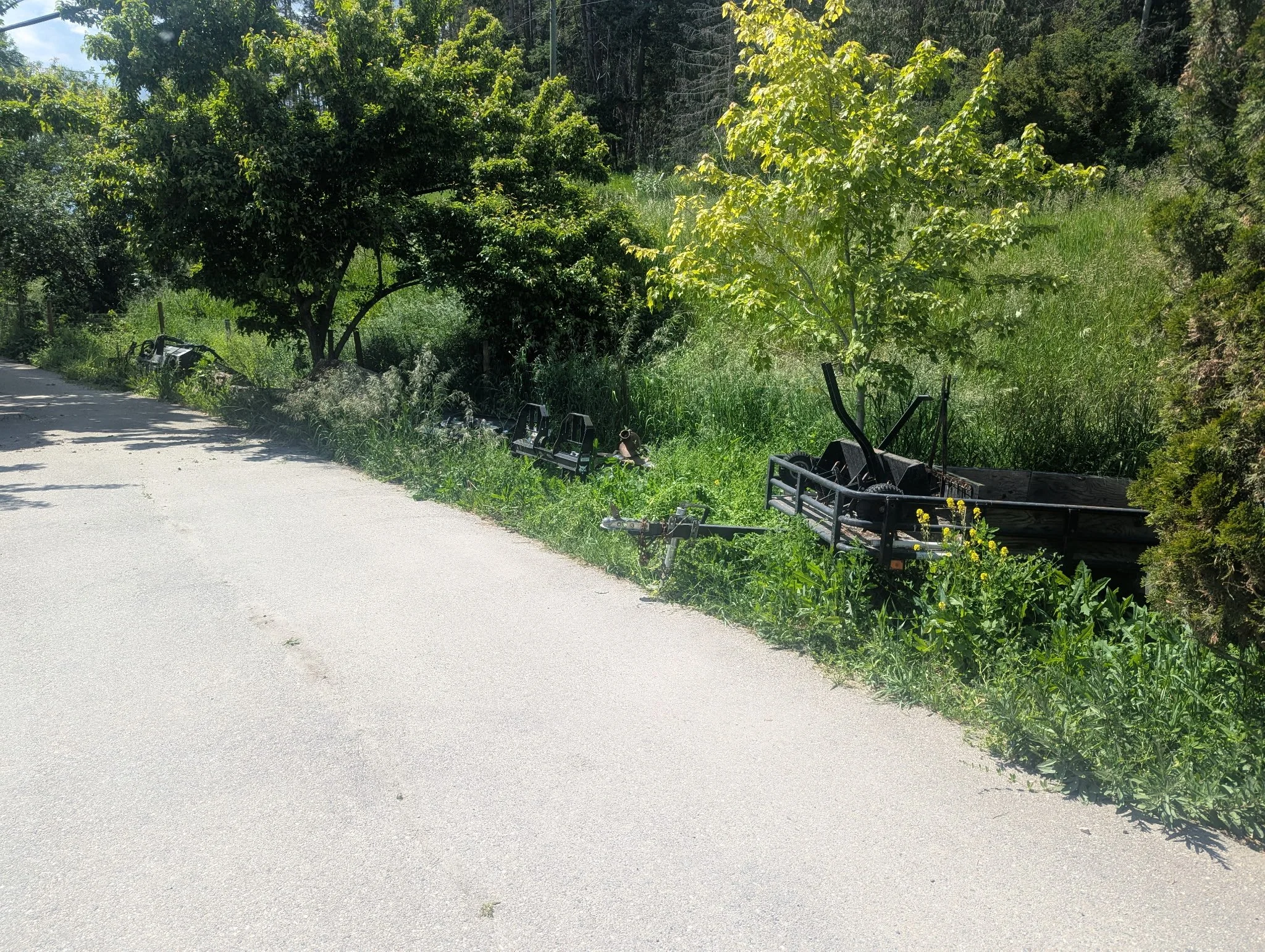 Debris and damaged trailers on the grassy roadside of a rural area with trees and vegetation.