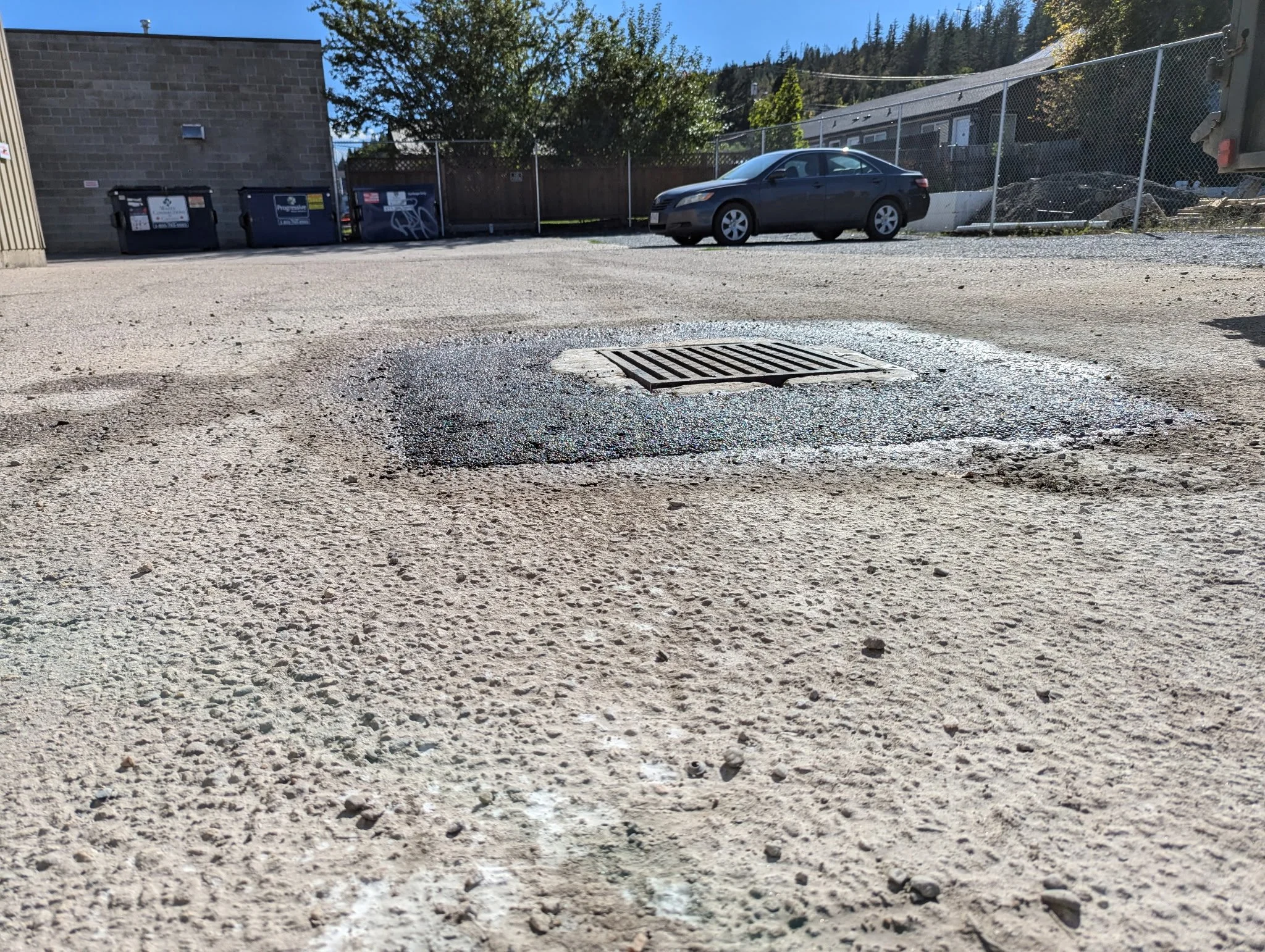 Close-up view of a concrete ground with a drain cover at the center, surrounded by a patch of black asphalt in an outdoor parking lot.
