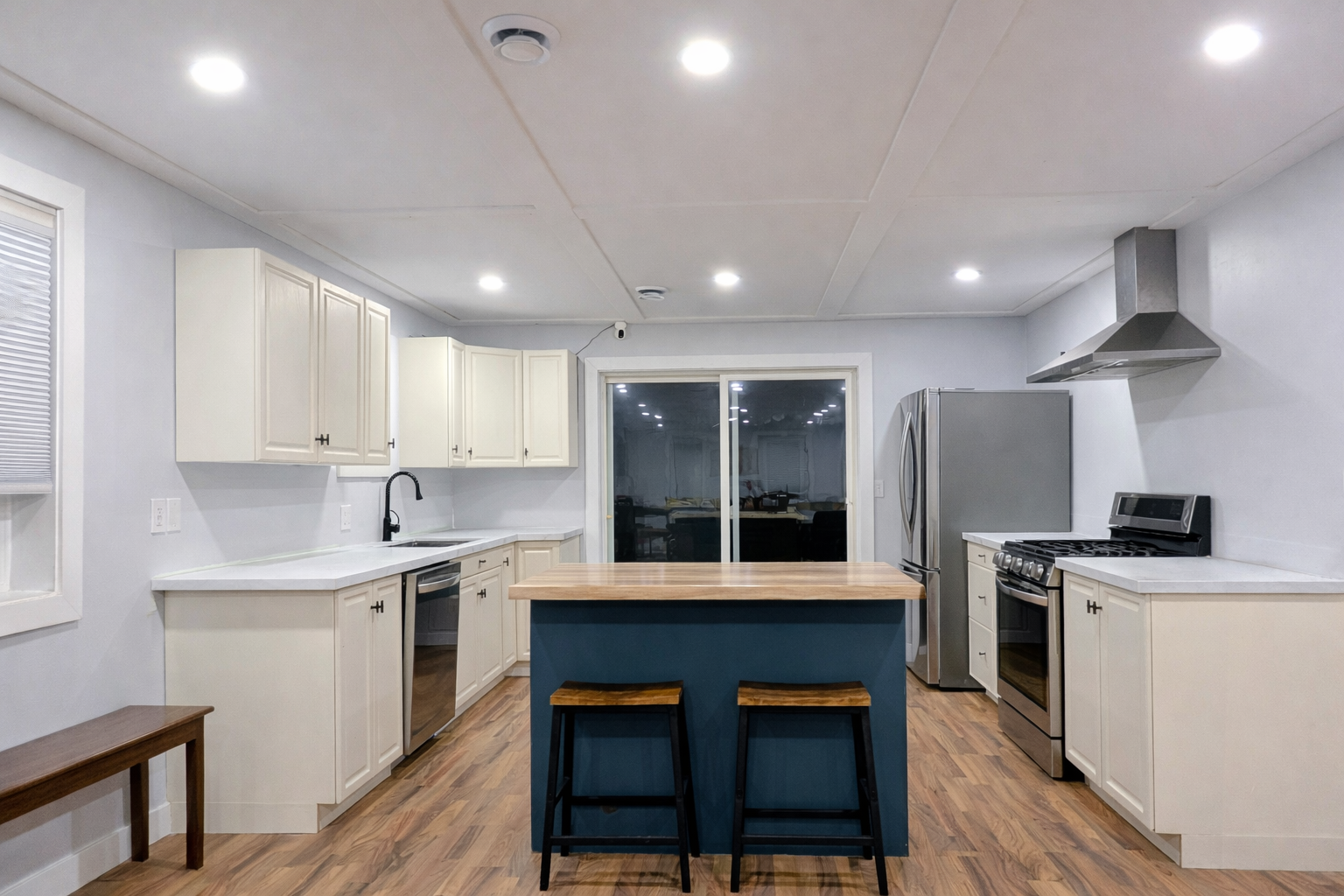 Modern kitchen with white cabinets, stainless steel appliances, a wooden island with two stools, and hardwood flooring.